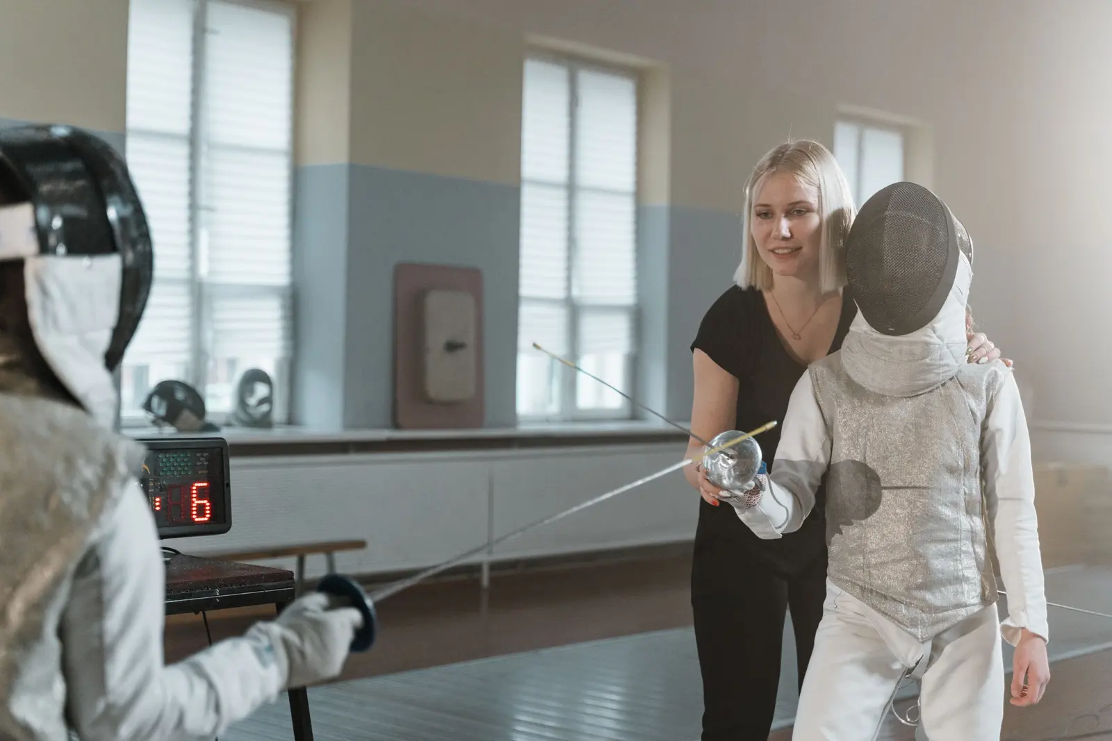 Maestra che guida il braccio di un giovane schermidore con la maschera