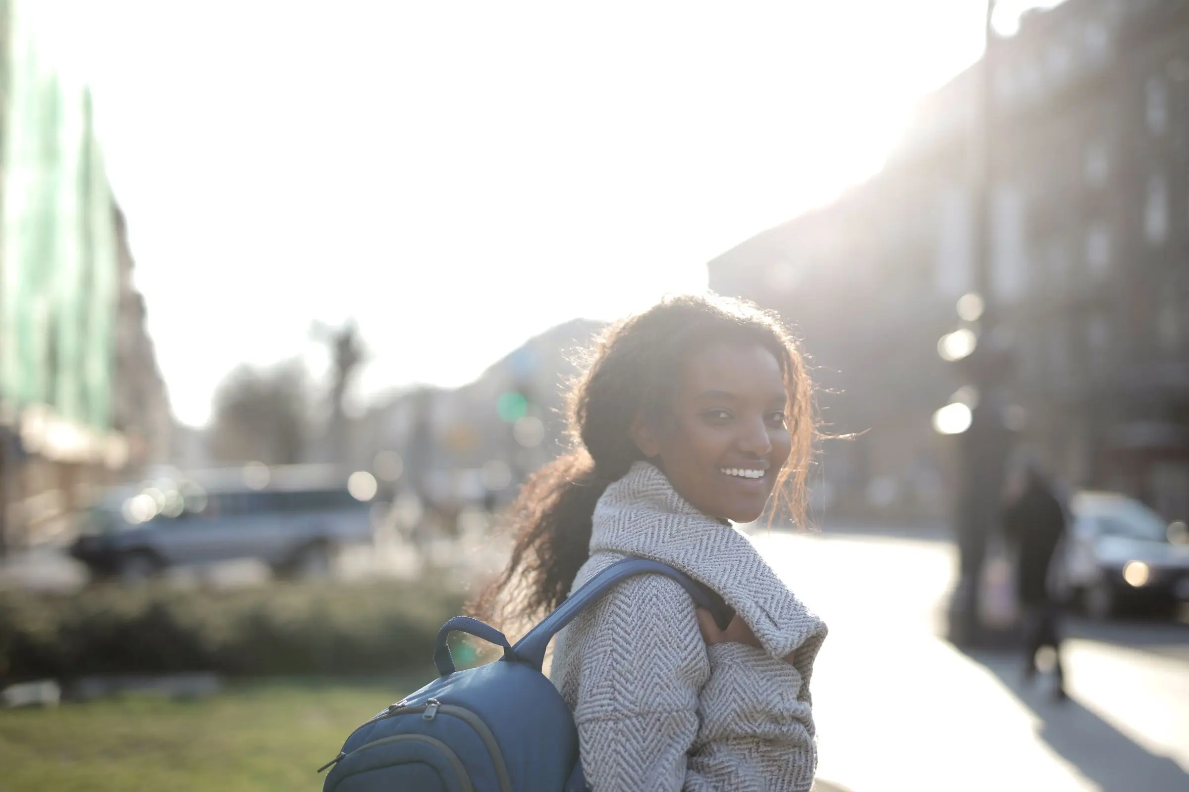 Una ragazza con lo zaino che si volta sorridendo in una strada di città, controluce