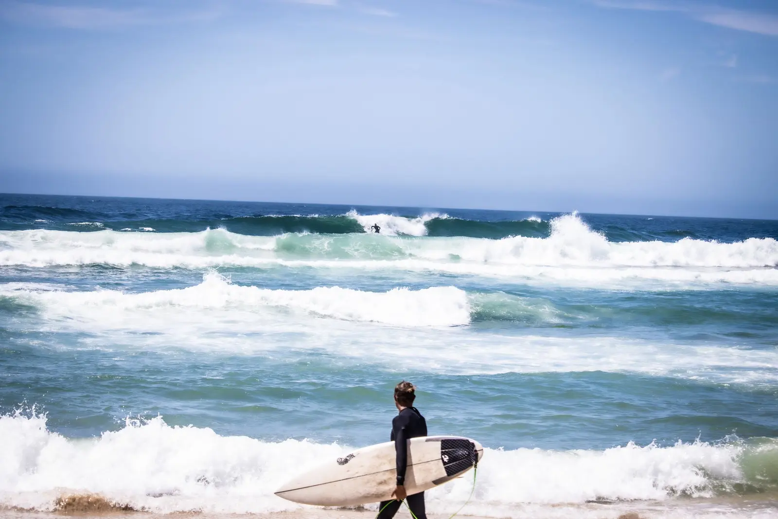 Un surfista lontano che cammina verso le onde con la tavola sottobraccio