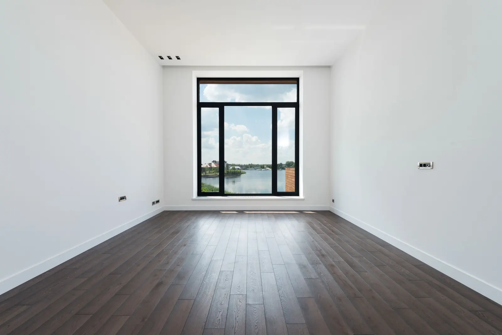 Una stanza vuota e luminosa con pareti bianche, pavimento in legno e una grande portafinestra