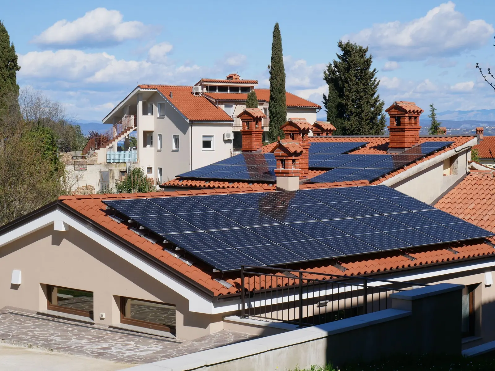 Case con tetti in coppi rossi e pannelli fotovoltaici, cipressi e colline sullo sfondo