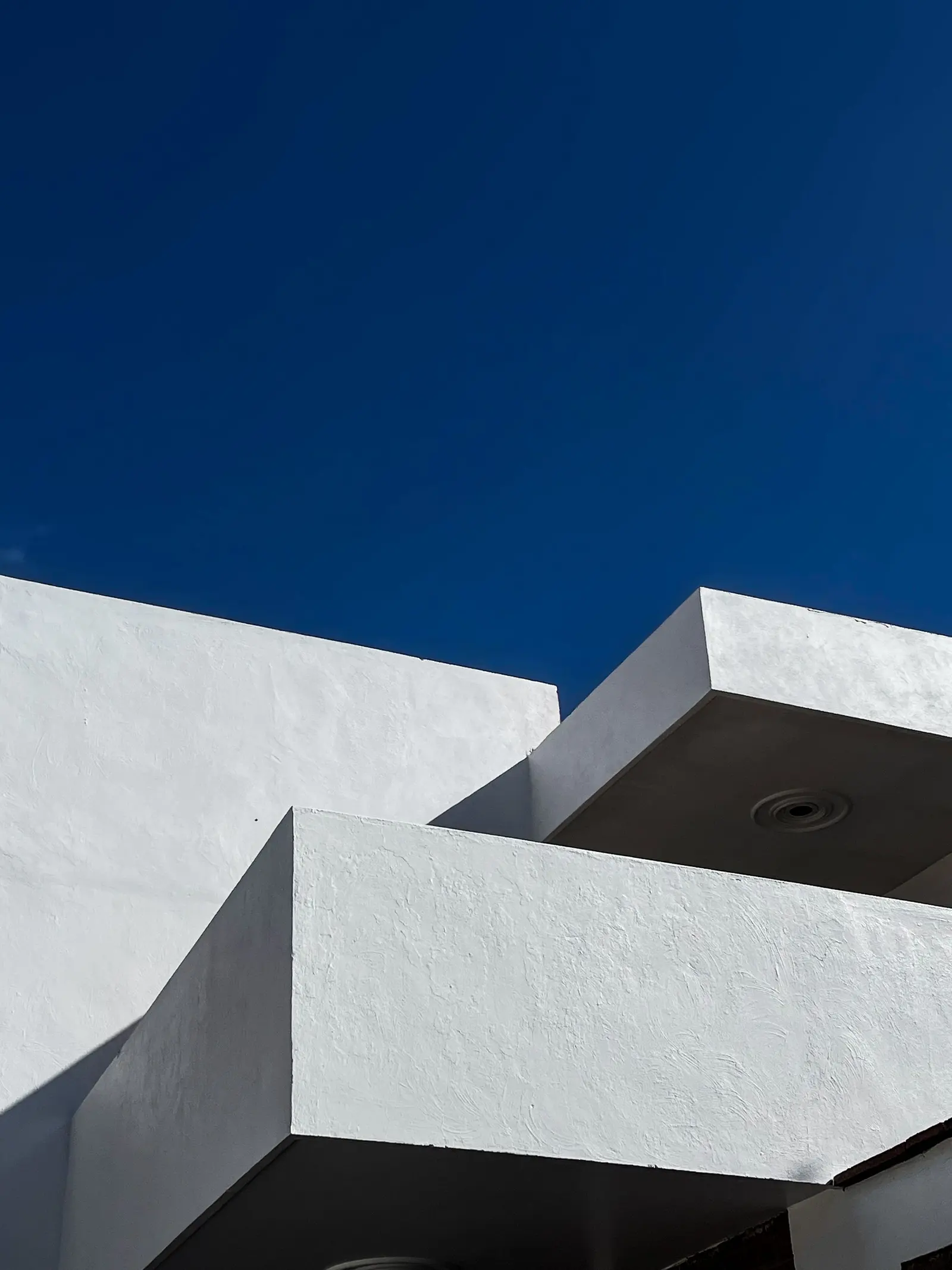 Balconi bianchi a sbalzo contro un cielo blu intenso; sotto il balcone più alto c’è un faretto incassato