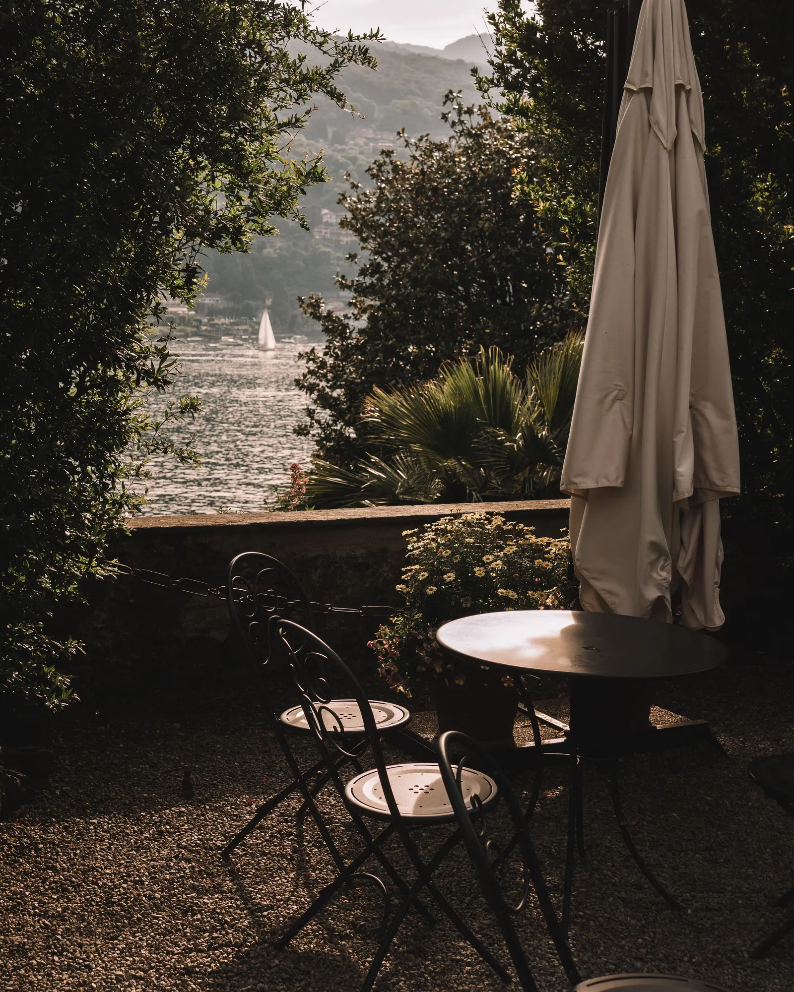 Terrazza in giardino con tavolino e sedie, il lago oltre le piante