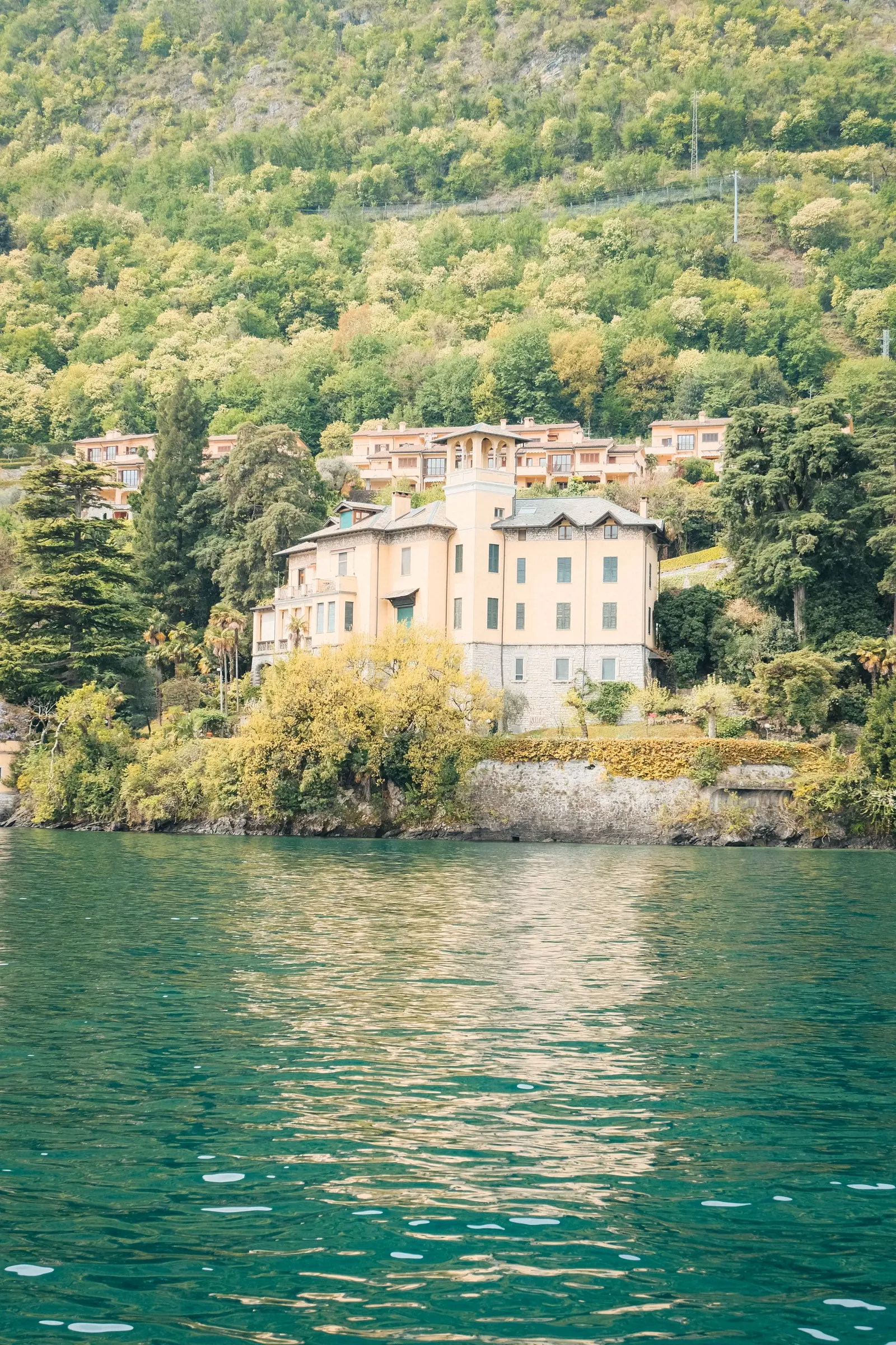 Casa d'epoca color rosa sulla riva, con la collina boscosa alle spalle