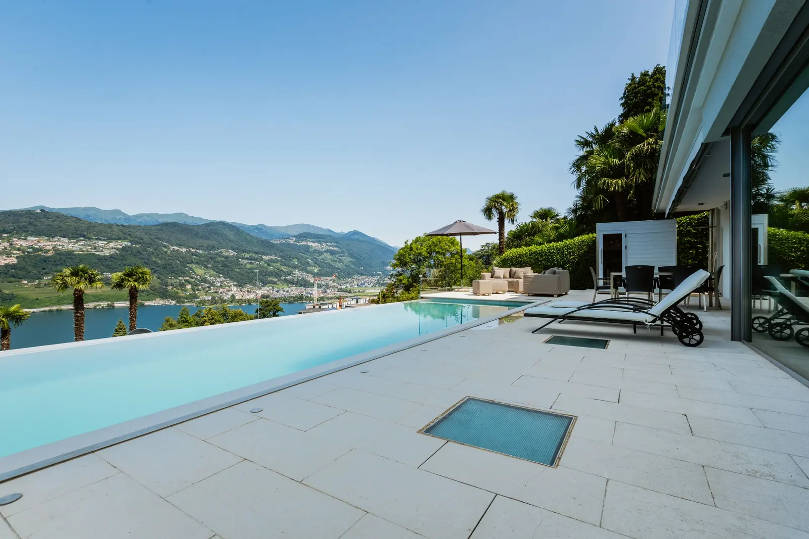 Piscina a sfioro sul lago con lettini e montagne sullo sfondo