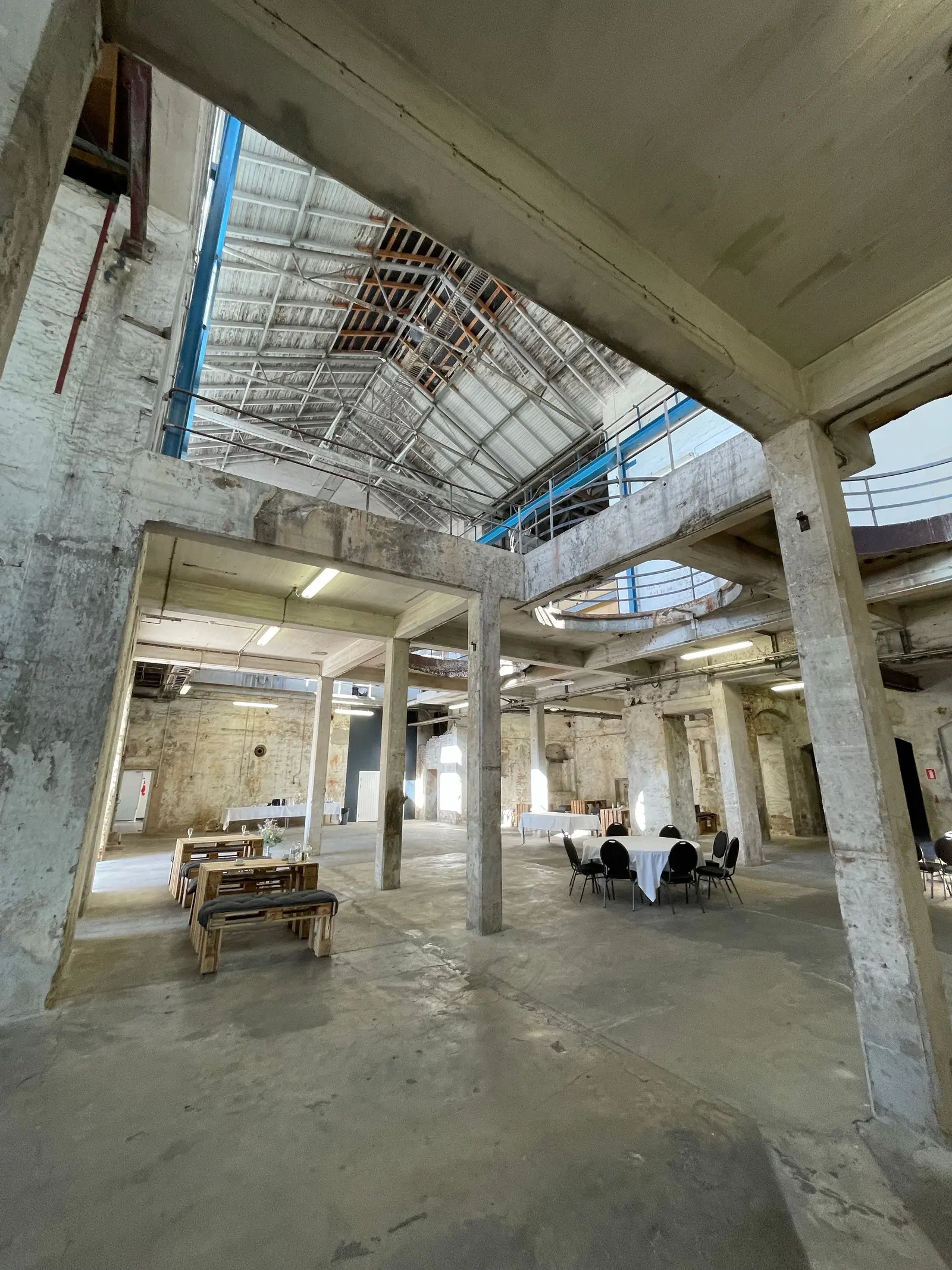 La grande sala dell'essiccatoio con pilastri in cemento e lucernari, allestita con tavoli per un incontro