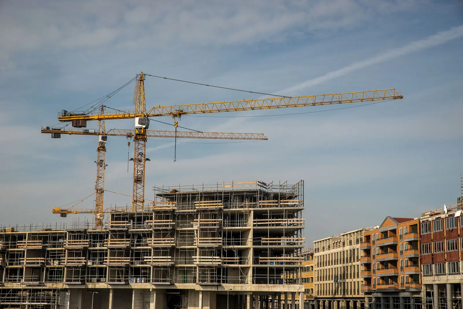 Due gru a torre gialle sopra una palazzina in costruzione avvolta dai ponteggi