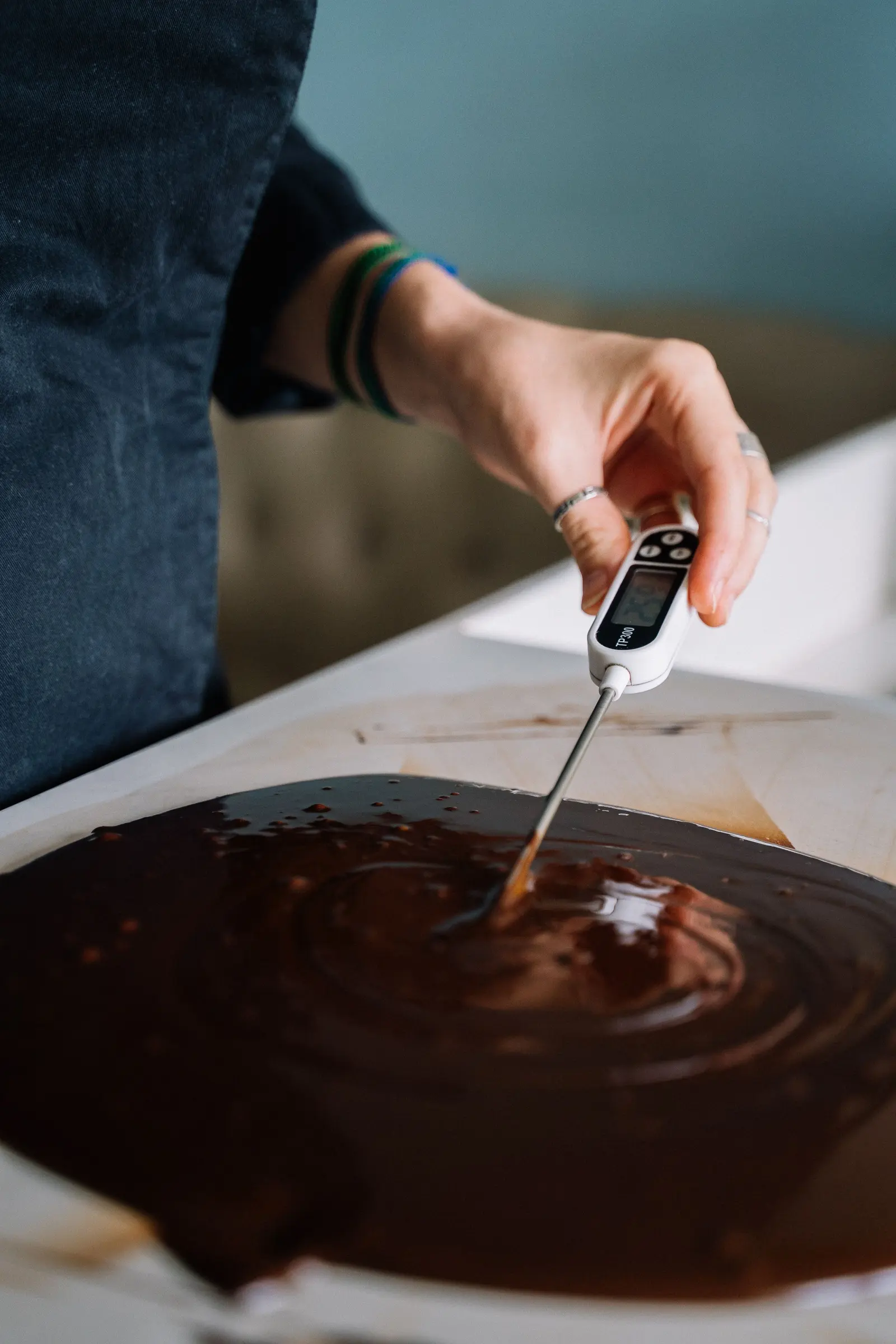 Una mano immerge il termometro nel cioccolato fuso steso sul banco