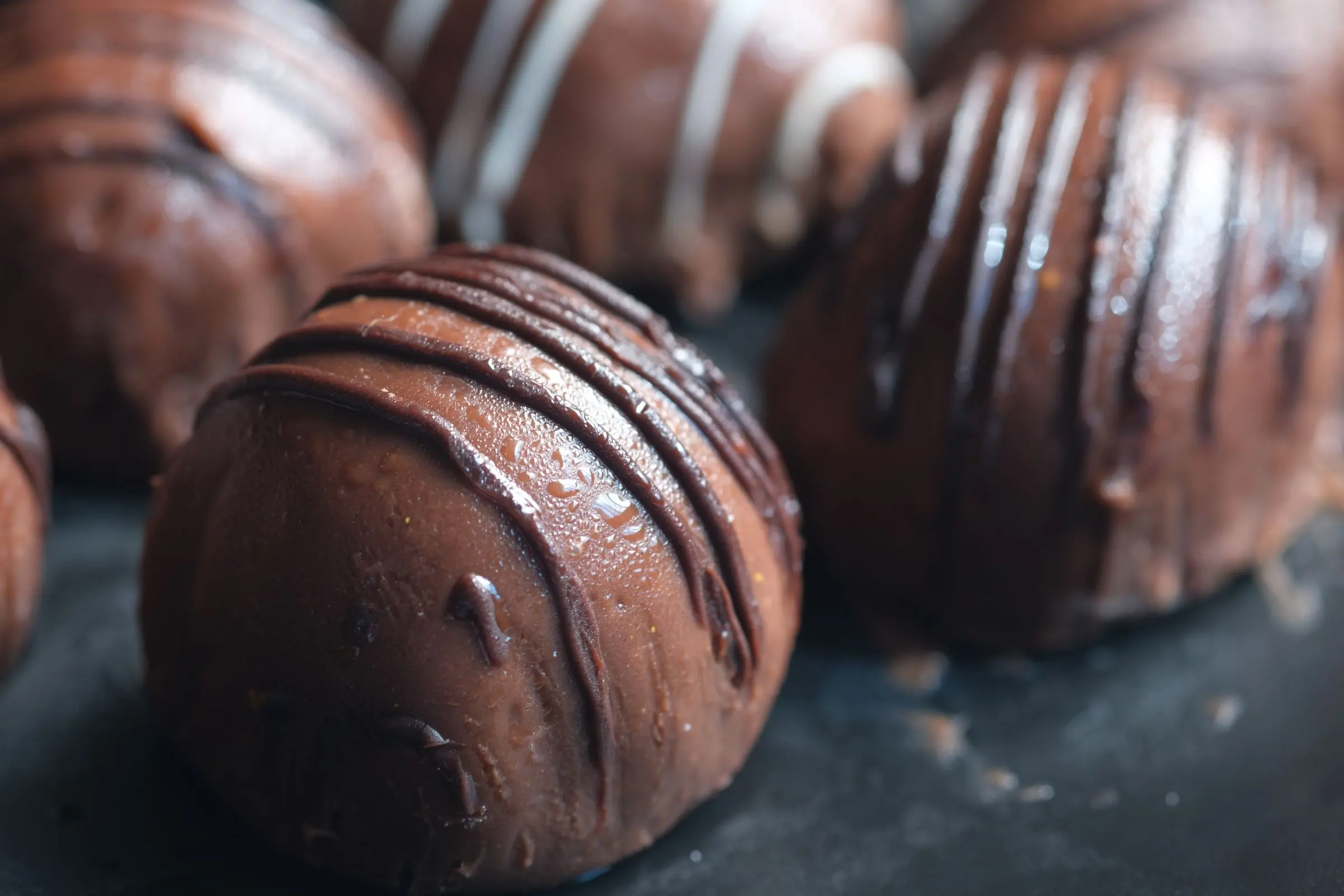 Tartufi di cioccolato fondente decorati con un filo di cioccolato, su fondo scuro