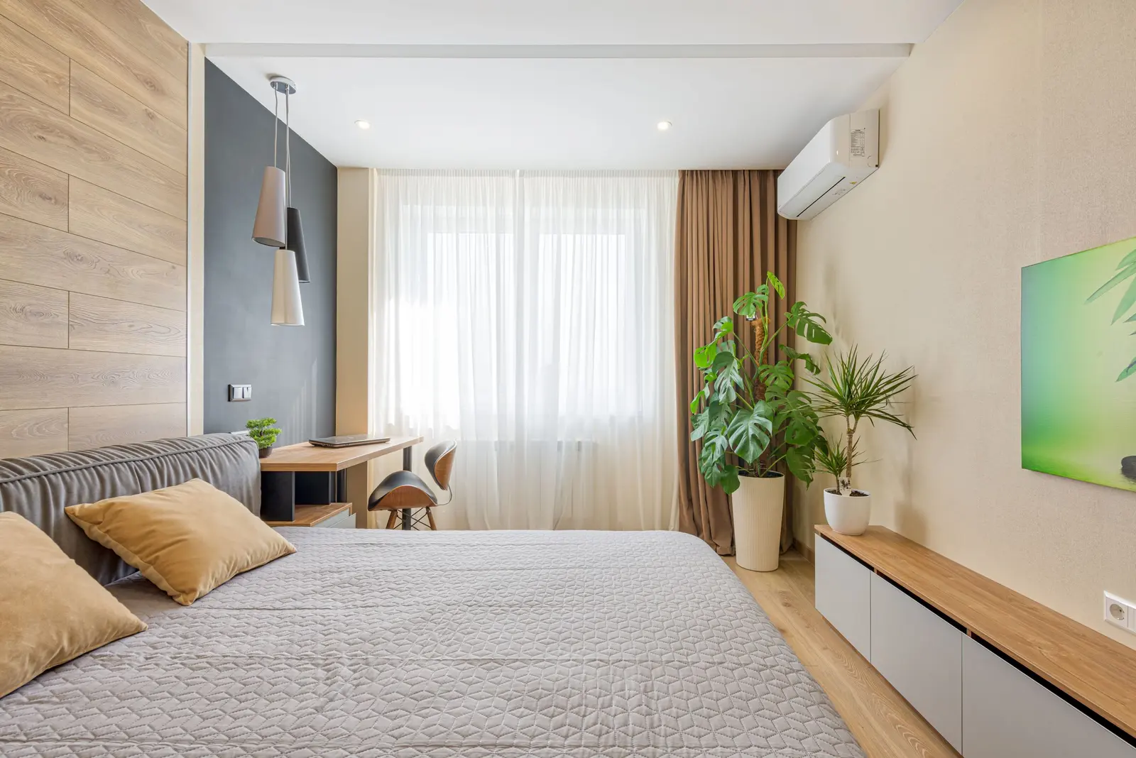 Una camera da letto chiara con lo split a parete sopra la tenda, piante e mobili in legno