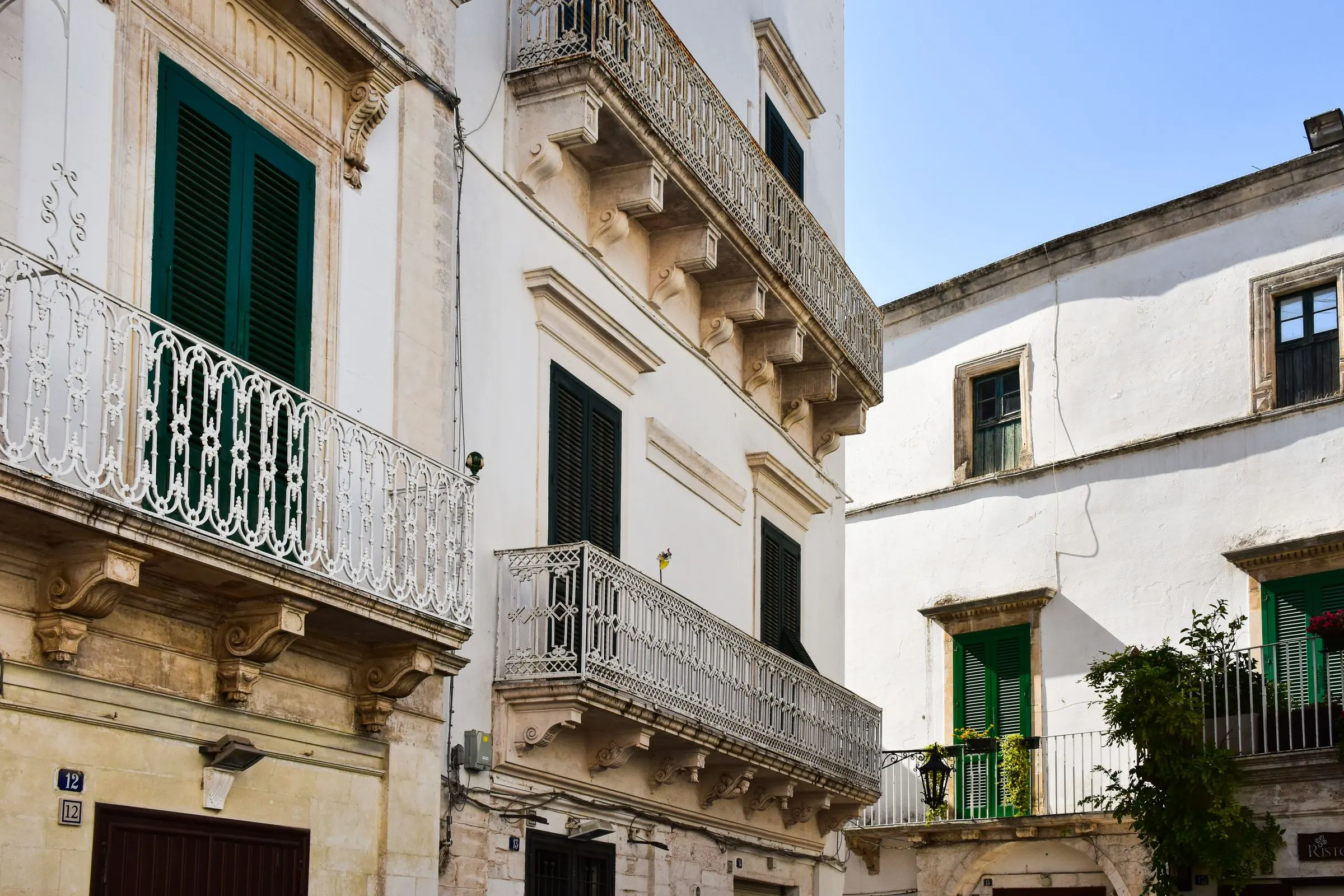 Palazzi bianchi del centro con balconi in ferro battuto e persiane verdi, in pieno sole