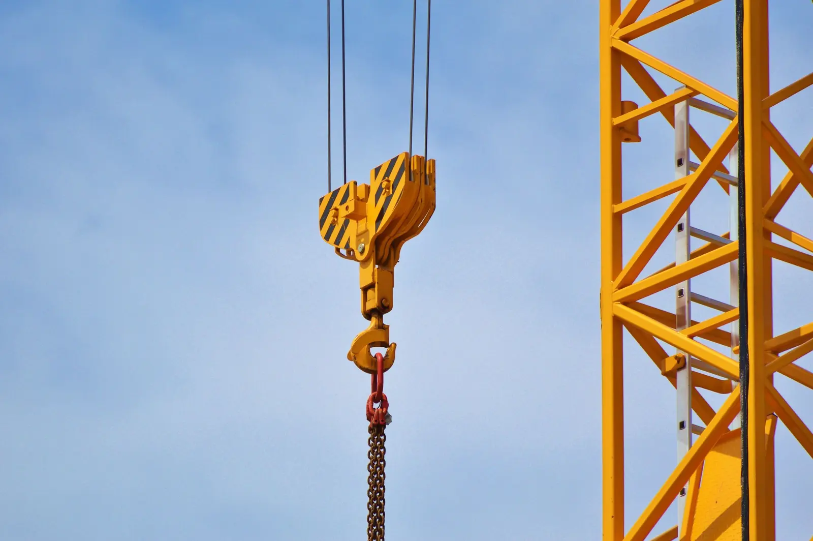 Il gancio giallo di una gru con la catena, accanto alla torre gialla, contro il cielo