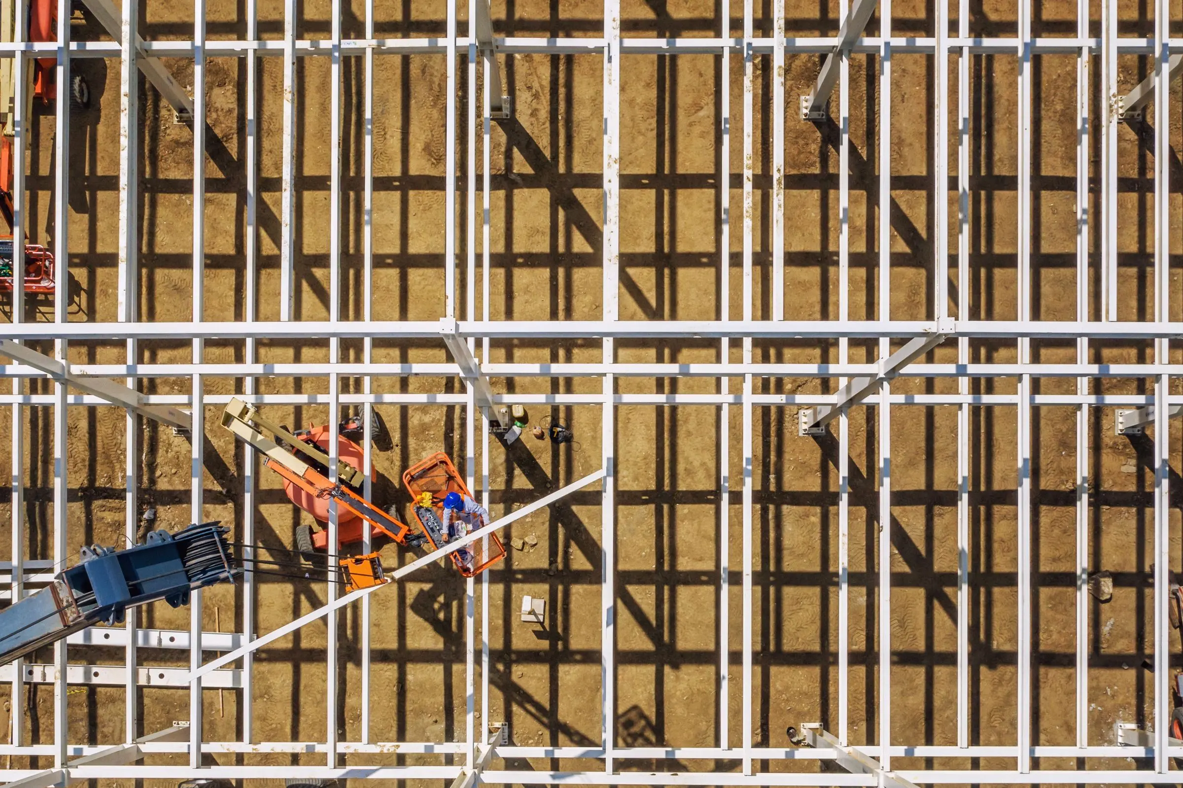 Il cantiere di un polo logistico visto dal drone: la struttura in acciaio sulla terra battuta, una piattaforma aerea e un operaio nel cestello