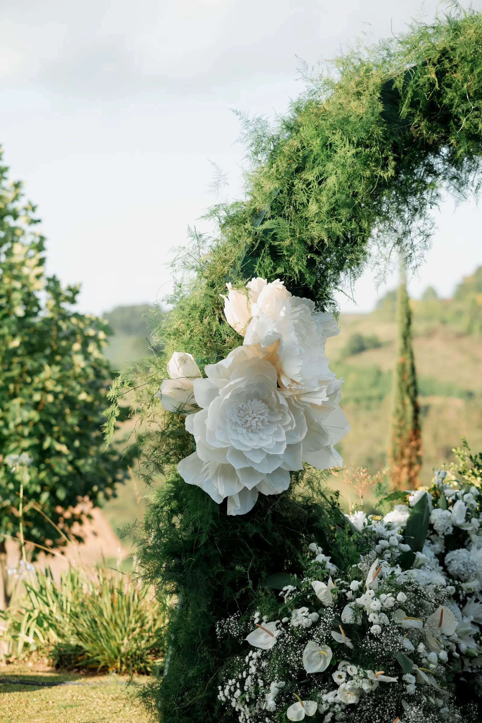 Un arco di fiori bianchi e foglie verdi all'aperto, con le colline sullo sfondo