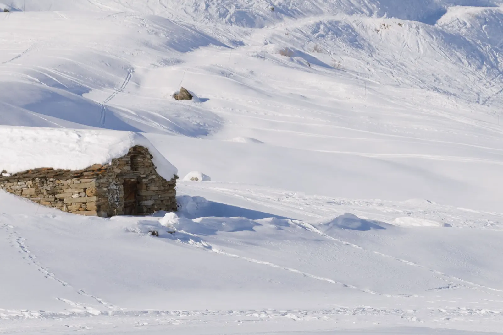 Una baita in pietra quasi sepolta dalla neve su un pendio