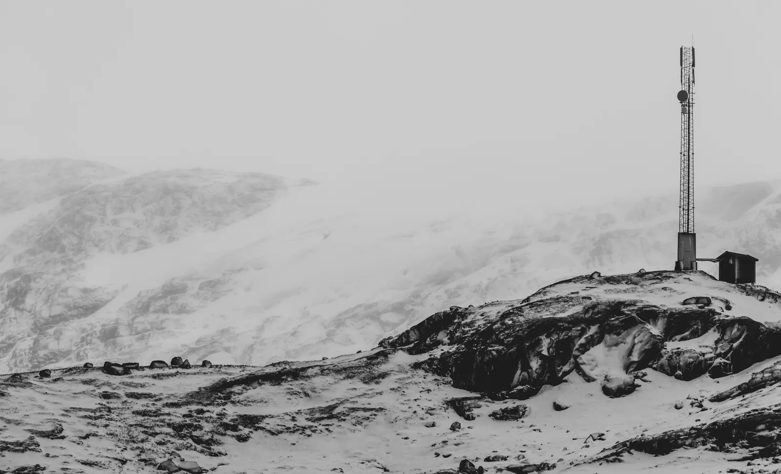 Una stazione ripetitrice isolata su un crinale coperto di neve, in bianco e nero