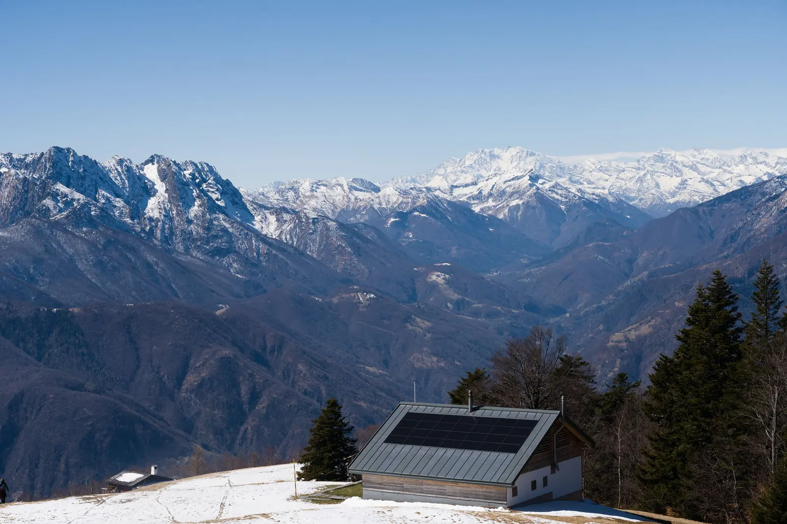 Una baita con i pannelli solari sul tetto, davanti a una valle alpina con le cime innevate