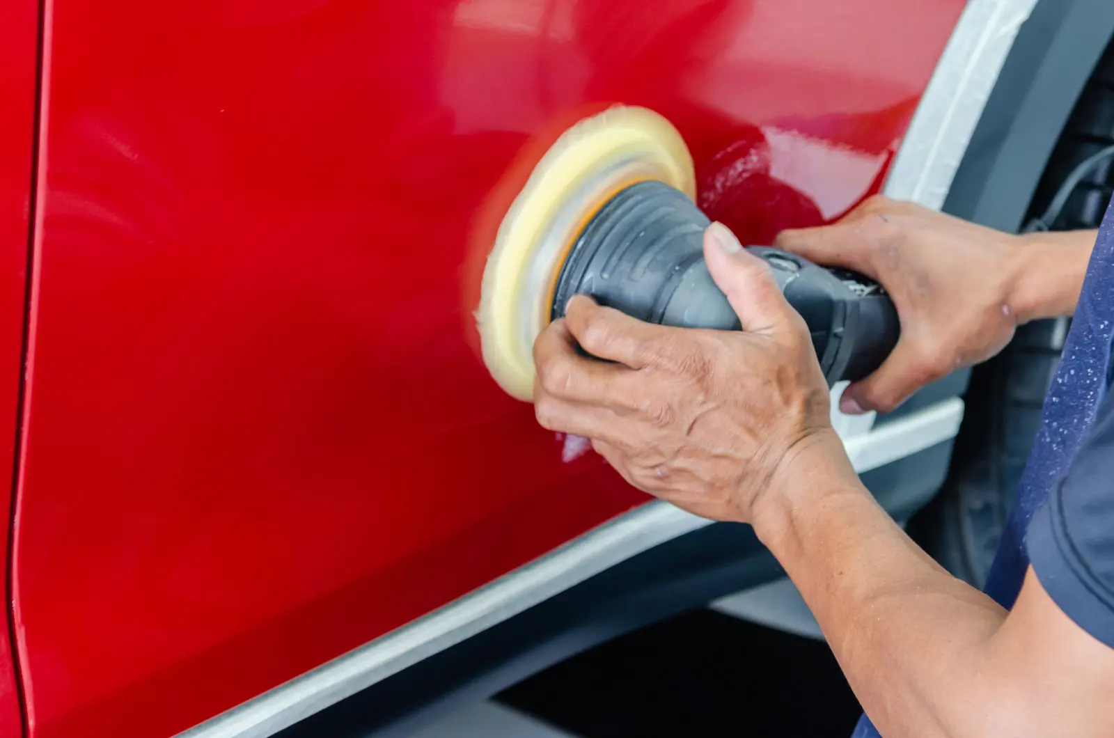 Mani che lucidano con la lucidatrice la fiancata rossa di un'auto