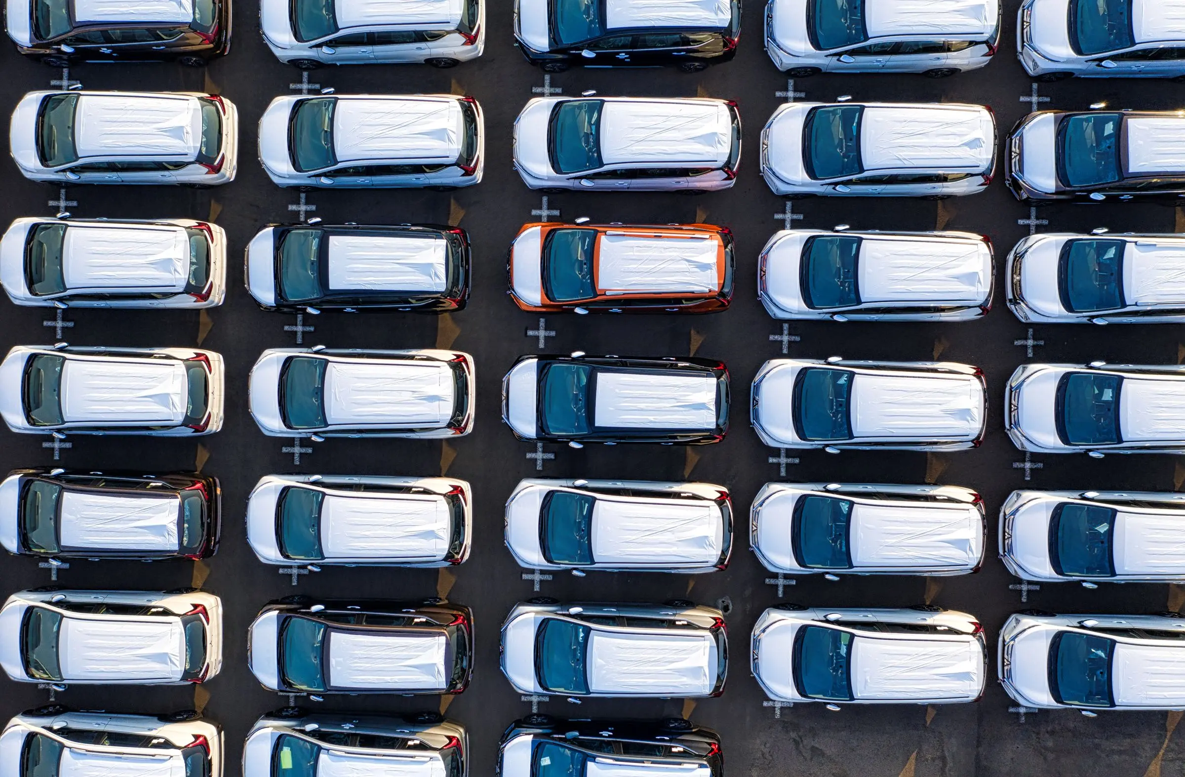 Piazzale visto dall'alto con auto parcheggiate in file ordinate, una arancione tra le bianche