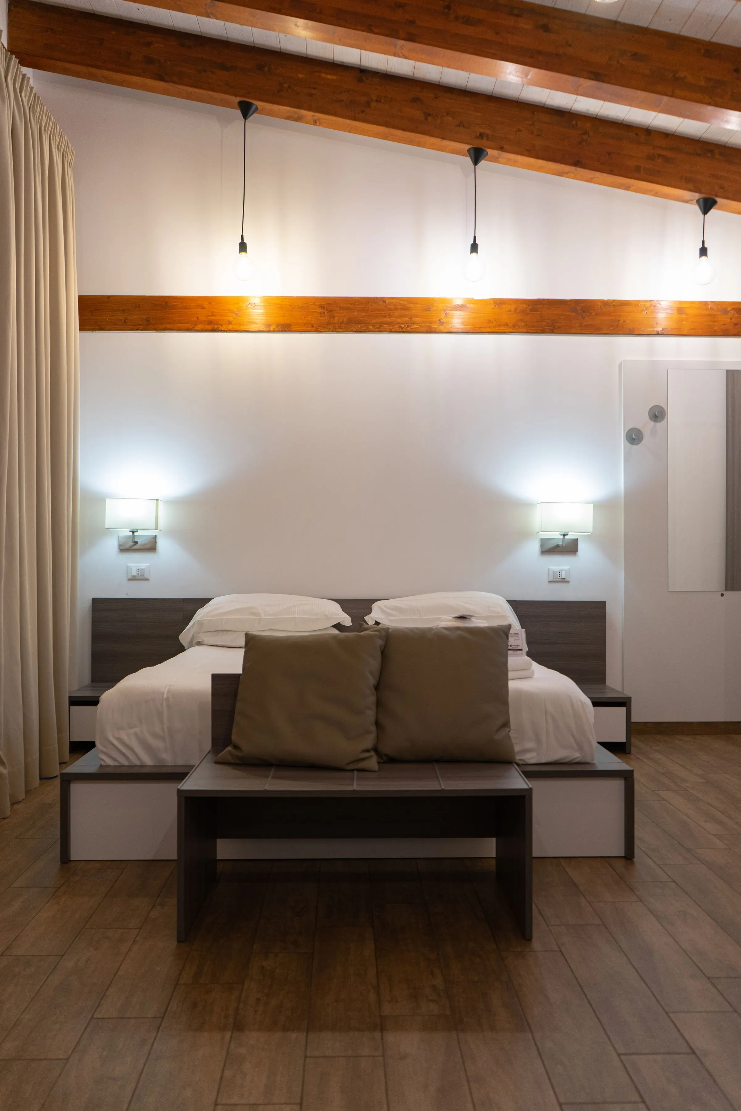 Camera da letto con travi in legno a vista, due lampade a sospensione e un letto basso