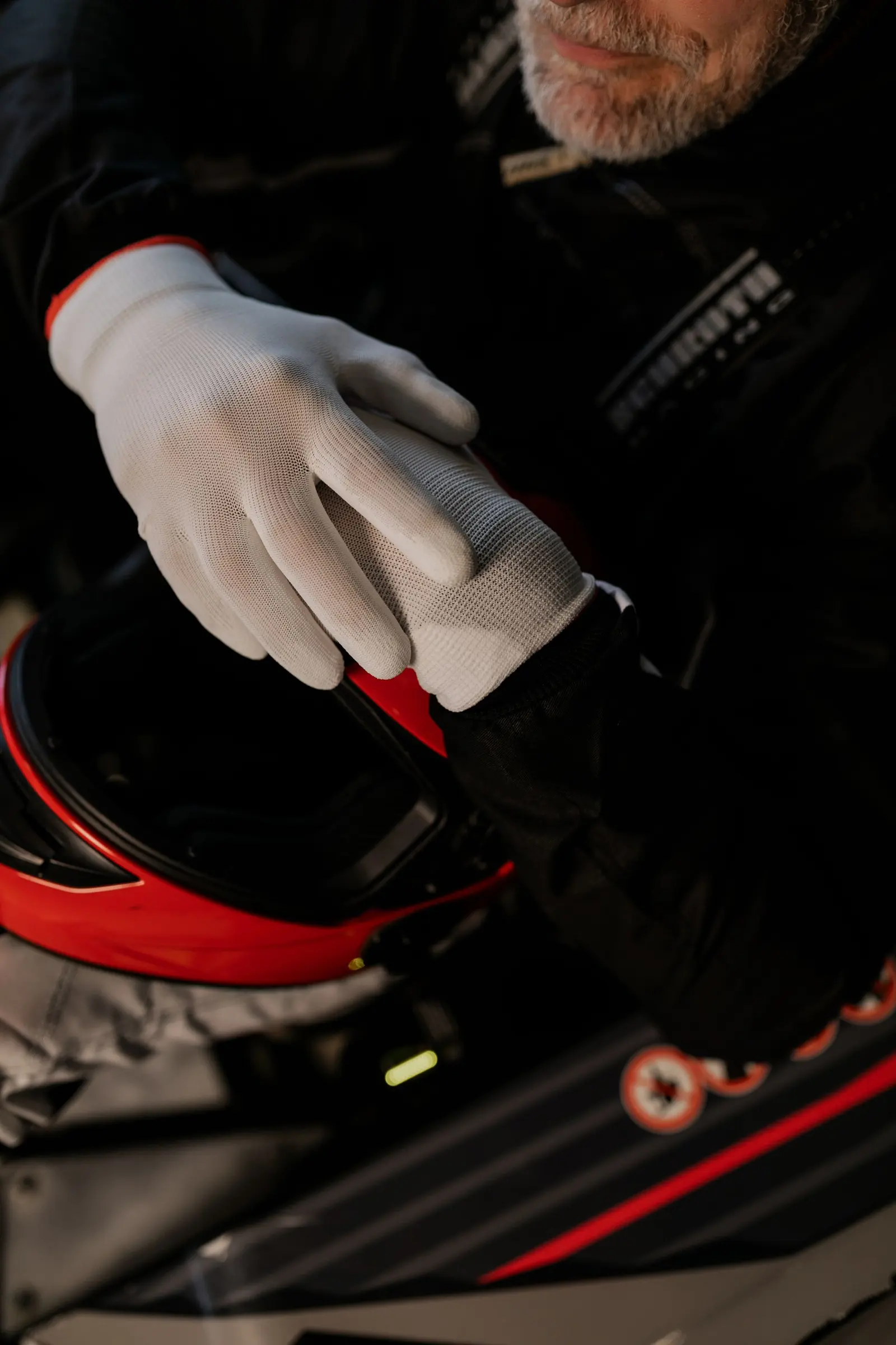 Mani con guanti bianchi che reggono un casco rosso e nero prima di salire in auto
