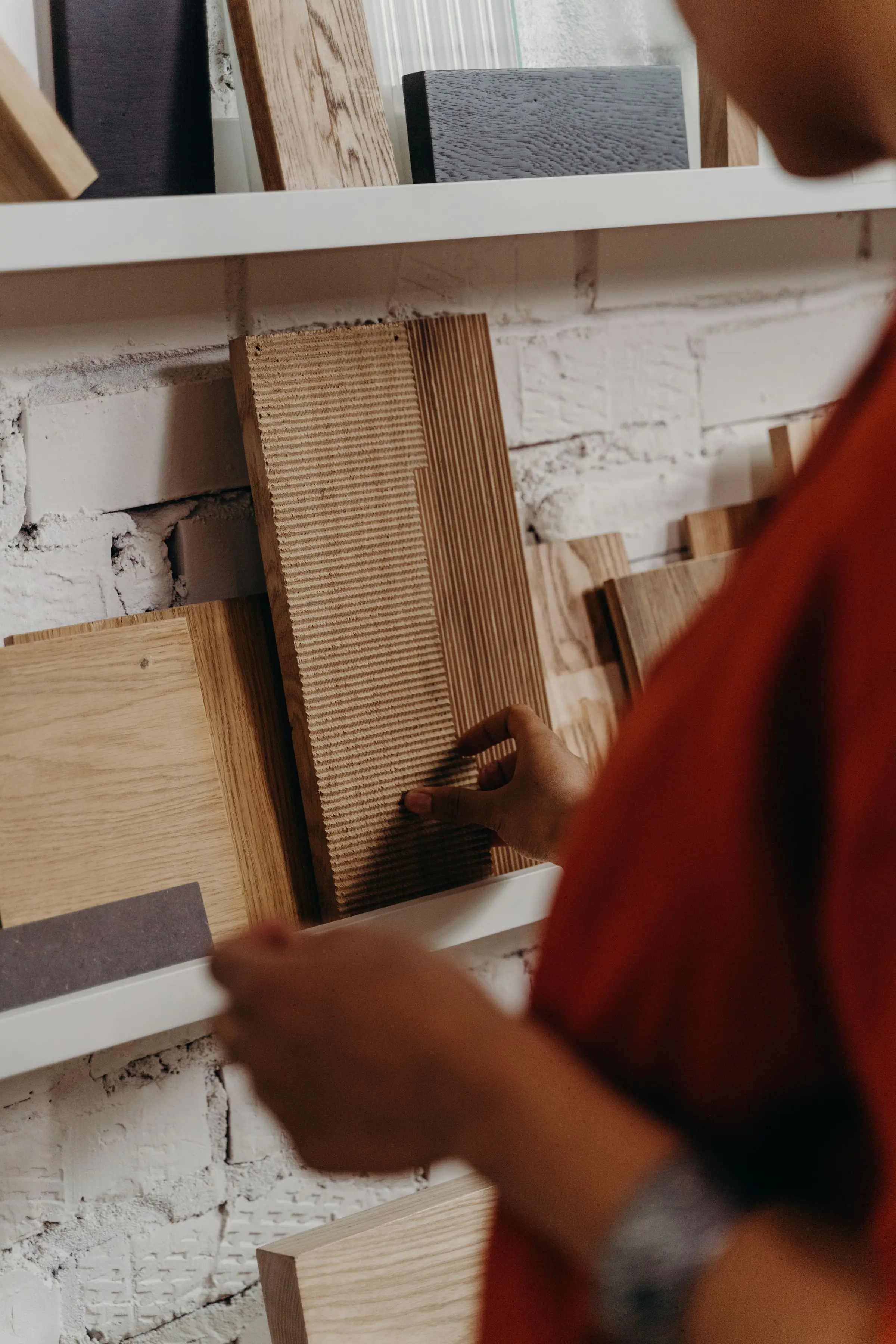 Una mano sceglie un listello di legno da una mensola piena di campioni