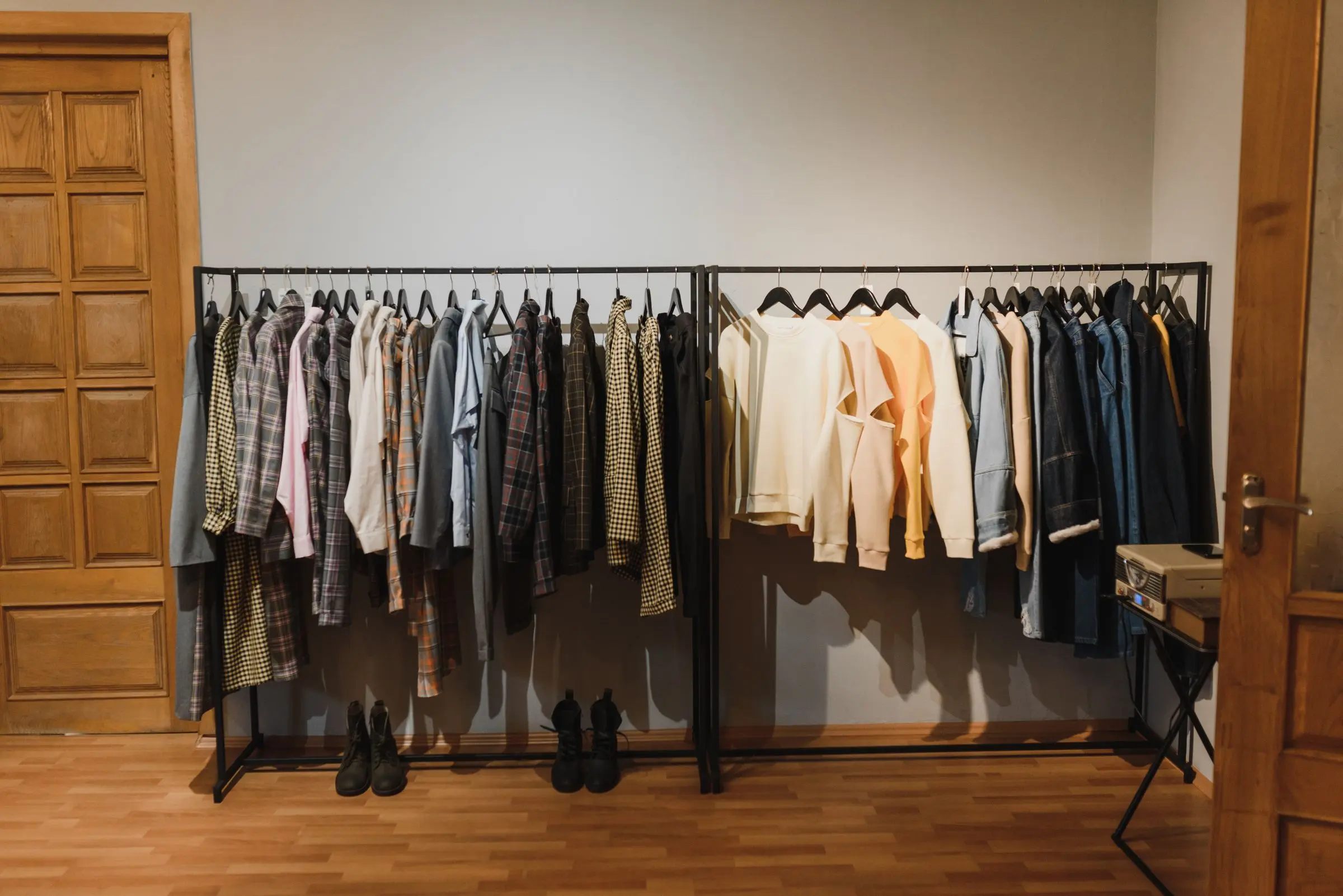 Sala con boiserie in legno e parquet, due stender metallici con maglie e camicie in toni neutri