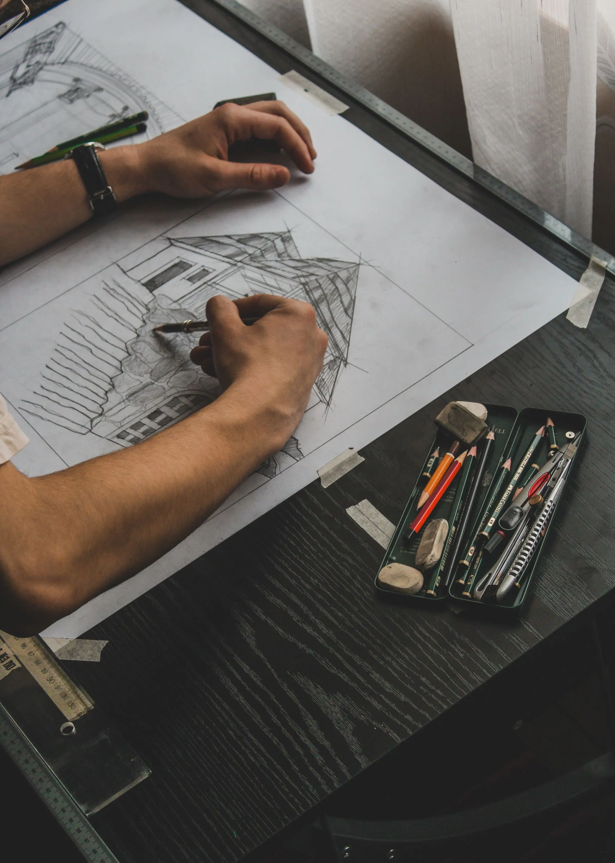 Mani che disegnano a matita su un foglio, su un tavolo nero con un astuccio di matite colorate