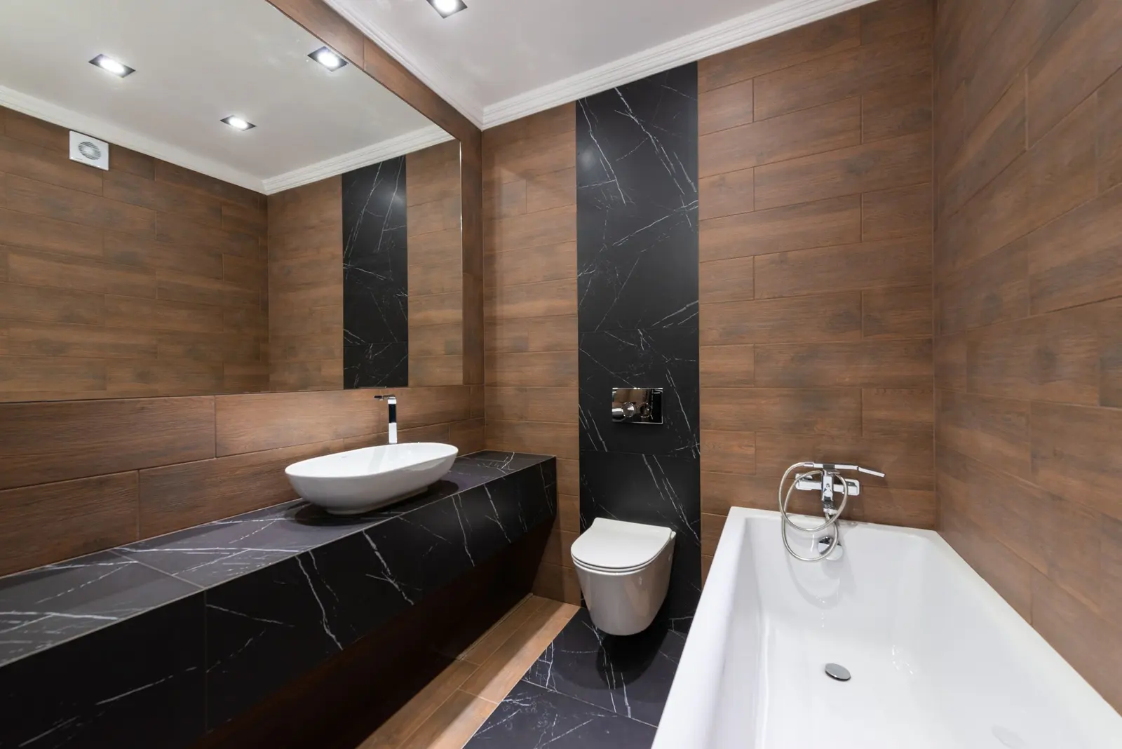 Bagno con pareti effetto legno, piano in pietra nera venata con lavabo d'appoggio e vasca