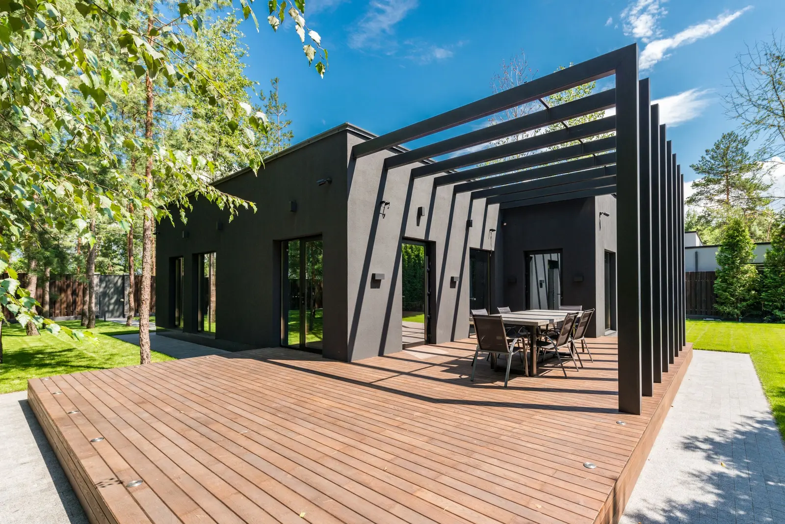 Pergola nera su una pedana di legno, con tavolo e sedie da esterno in mezzo al giardino