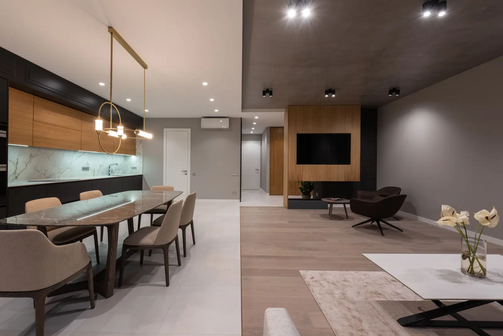 Open space allestito: tavolo lungo in pietra con sedie imbottite, cucina in legno sul fondo