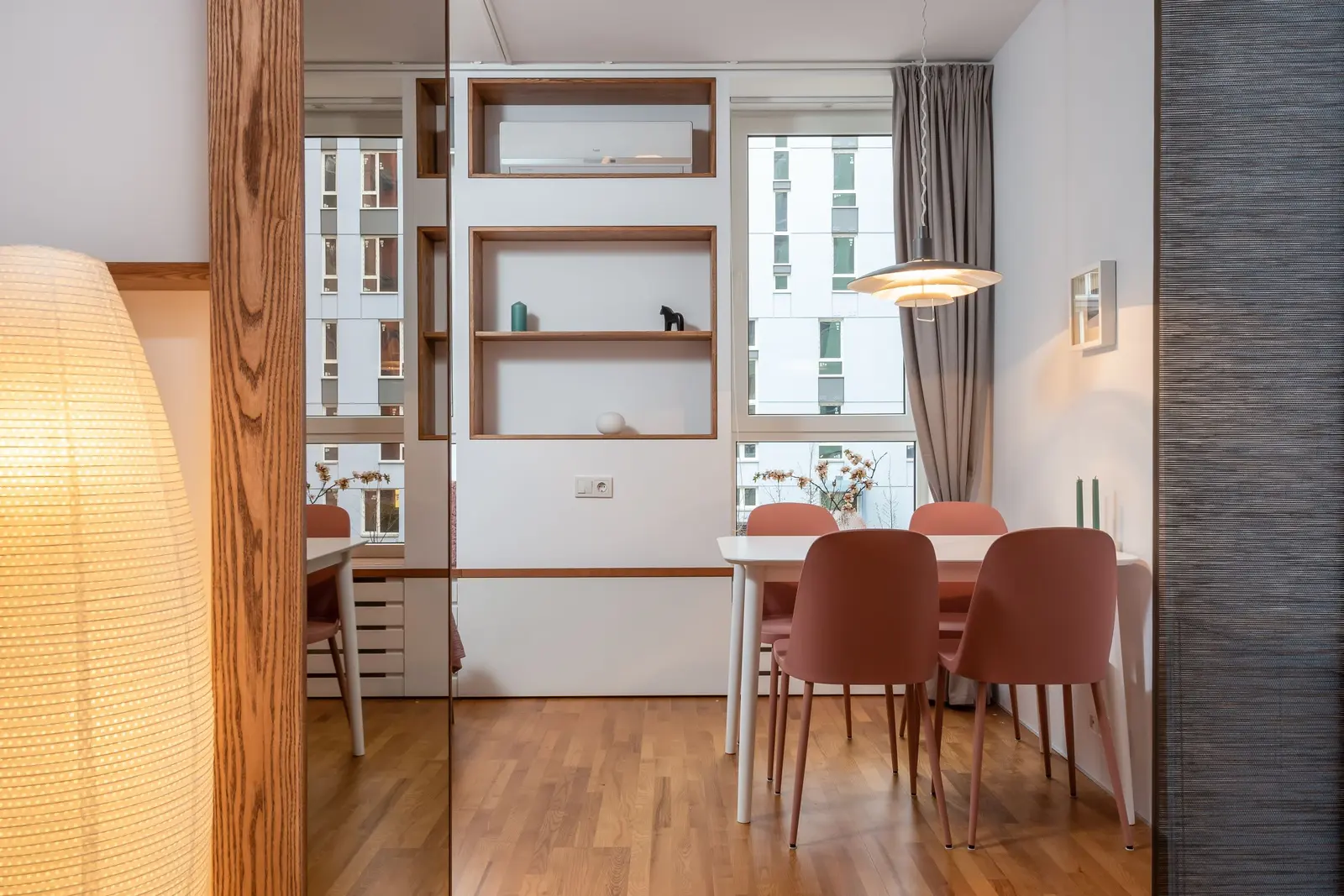 Angolo pranzo con sedie color terracotta, una libreria bianca a vani e una lampada di carta in primo piano