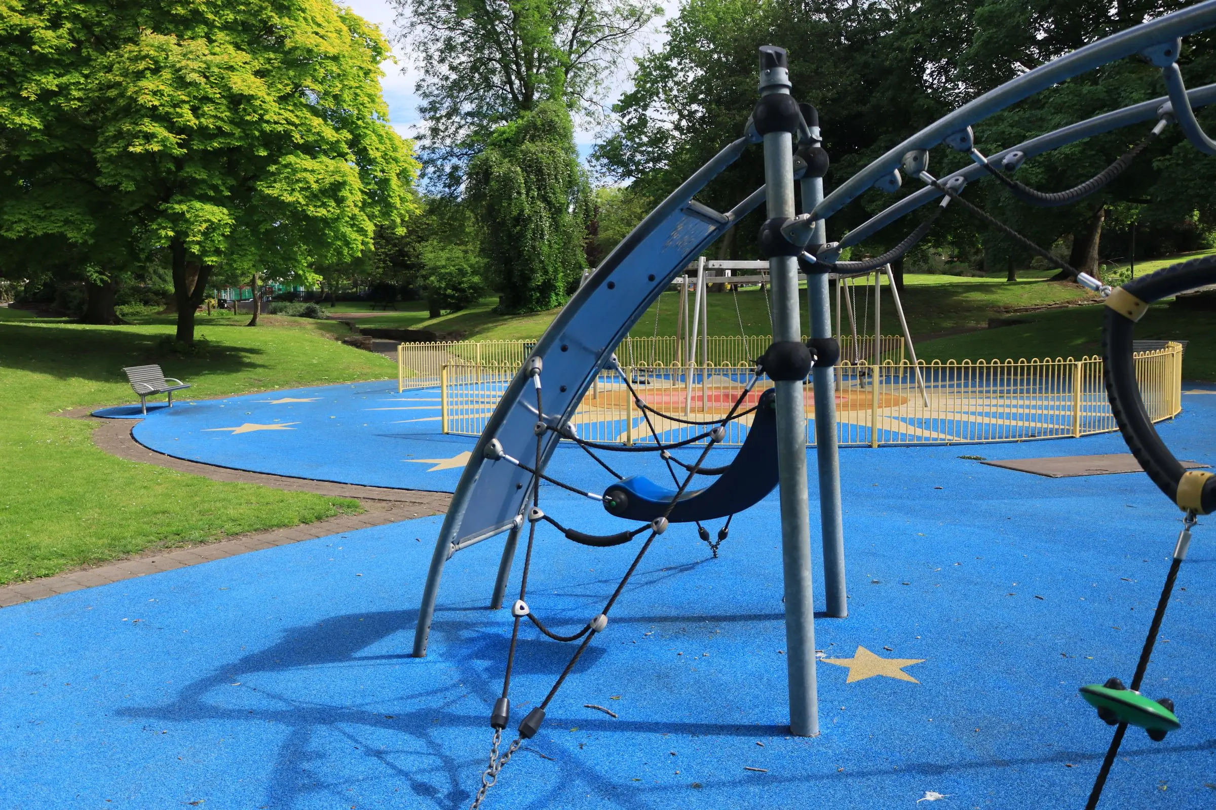 Struttura d'arrampicata a funi su una pavimentazione colata blu con stelle, in un parco con grandi alberi