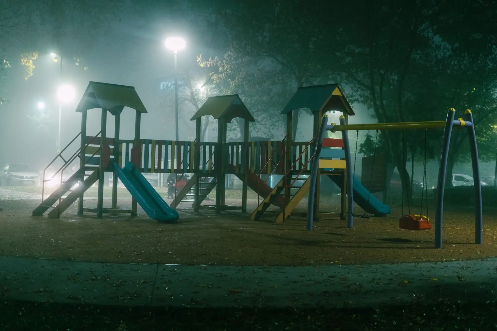 Area giochi di sera nella nebbia, con i lampioni accesi e le strutture in legno