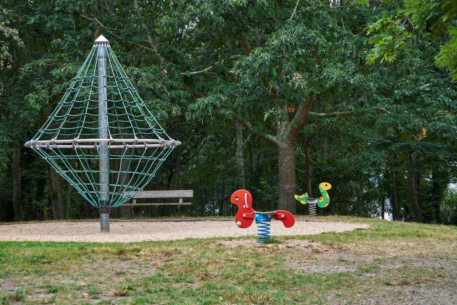 Piramide di funi in un parco alberato, con due giochi a molla colorati vicino
