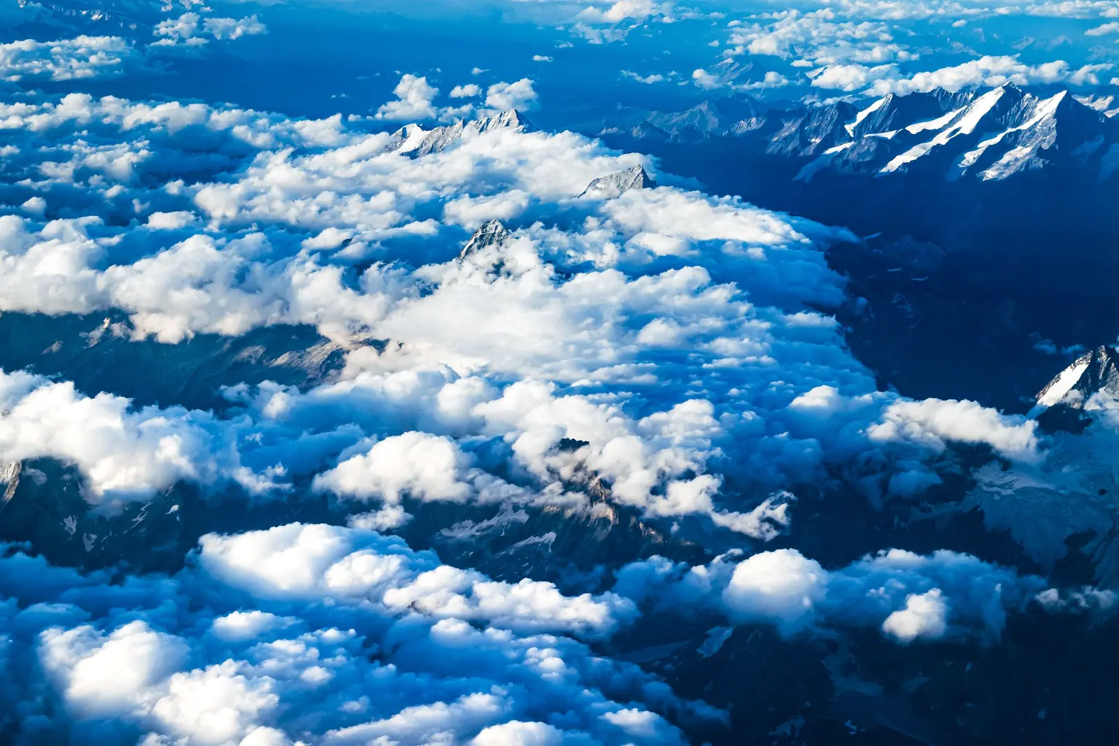 Le Alpi dall'alto, cime innevate tra le nuvole bianche e il cielo blu