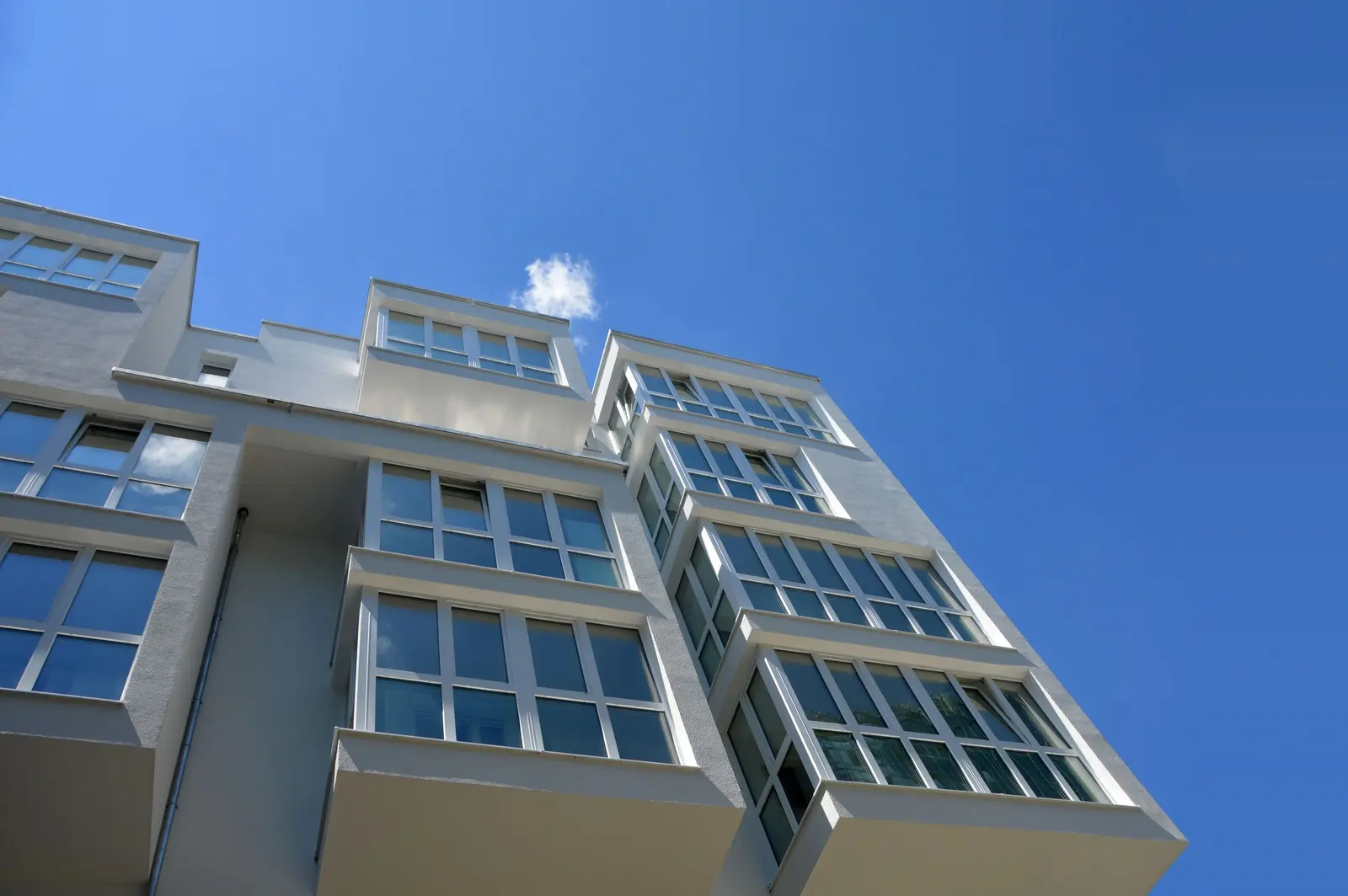 Dopo: una palazzina nuova con l'intonaco bianco e i bovindi vetrati, vista dal basso contro il cielo blu