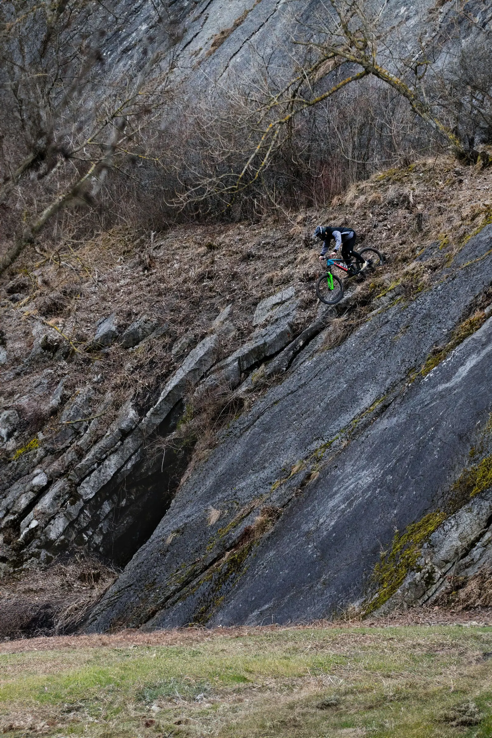 Un rider scende una placca di roccia ripida tra gli alberi spogli