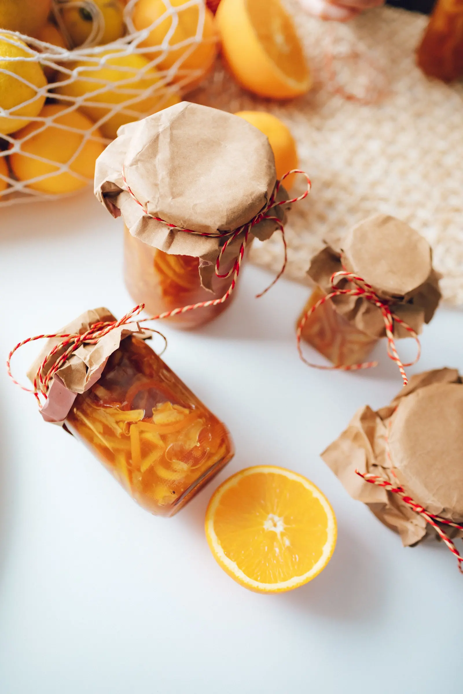 Vasetti di marmellata d'arance chiusi con carta e spago, arance tagliate accanto