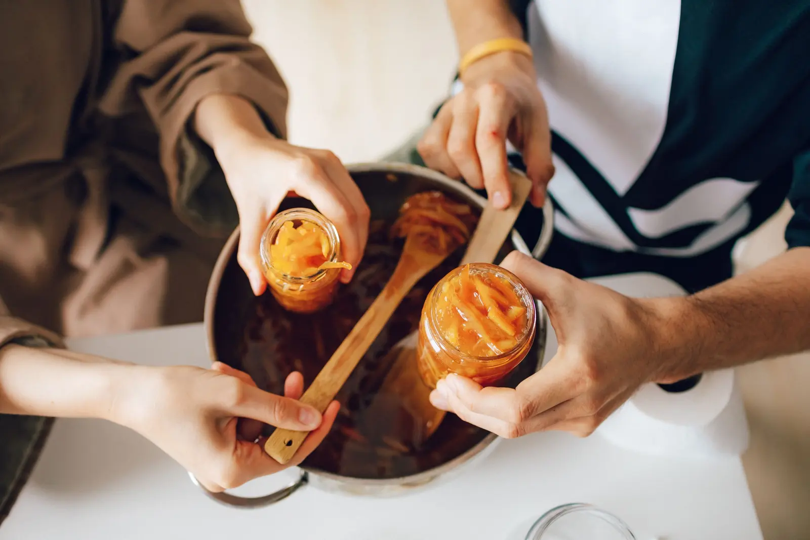 Due persone riempiono i vasi di marmellata d'arance dalla pentola con un cucchiaio di legno