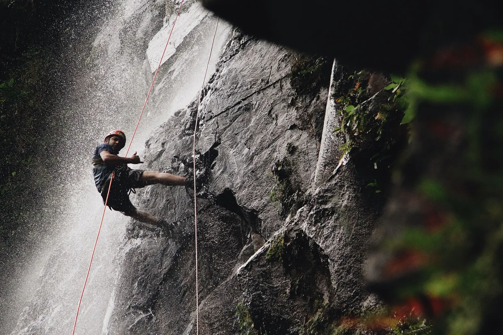 Una persona si cala in corda dentro una cascata, in controluce contro la roccia