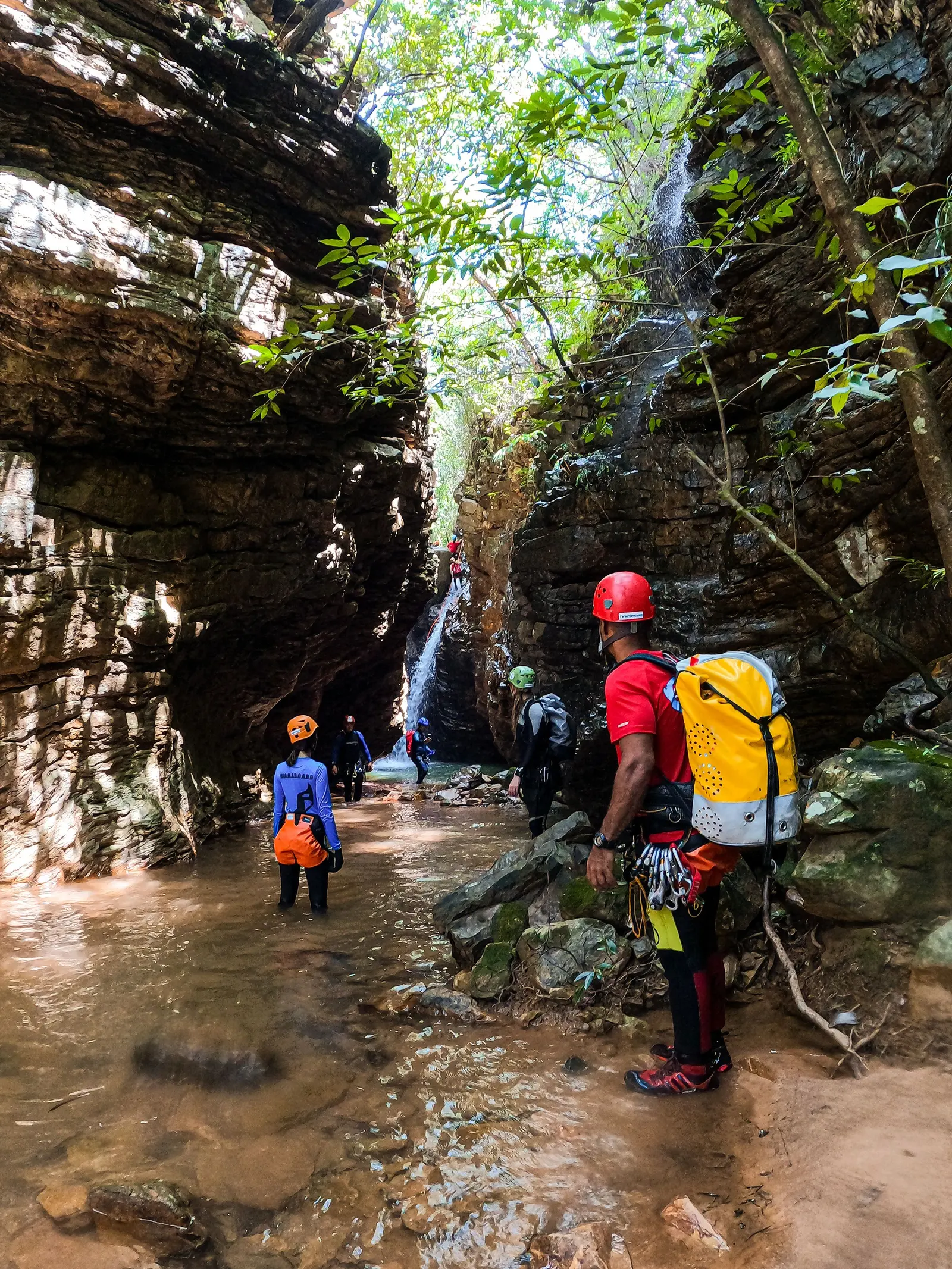 Un gruppo con il casco che cammina nell'acqua del torrente dentro una forra stretta