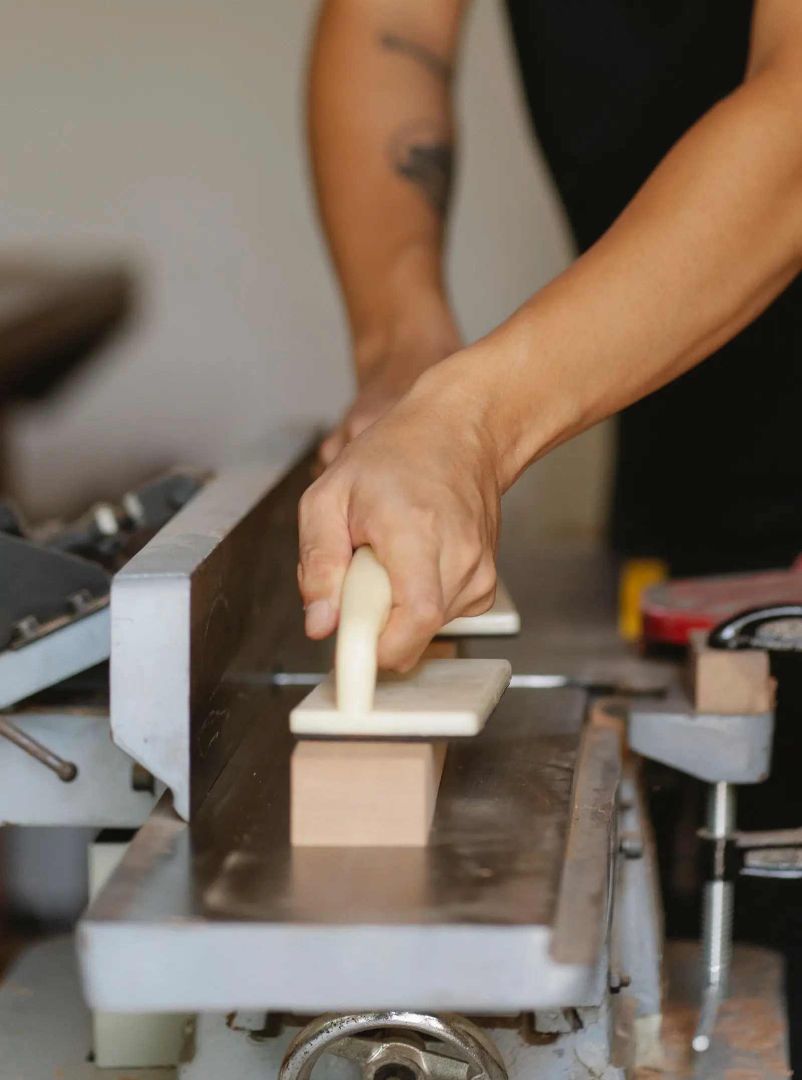 Due mani spingono un pezzo di legno sulla pialla a filo con lo spingitoio