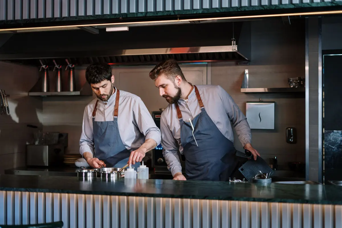 Due cuochi con il grembiule al lavoro in una cucina a vista