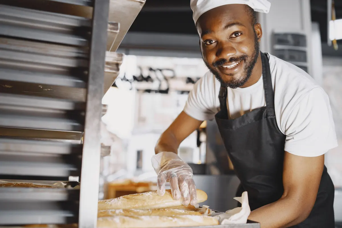 Un panettiere sorridente con guanti monouso sistema il pane appena sfornato