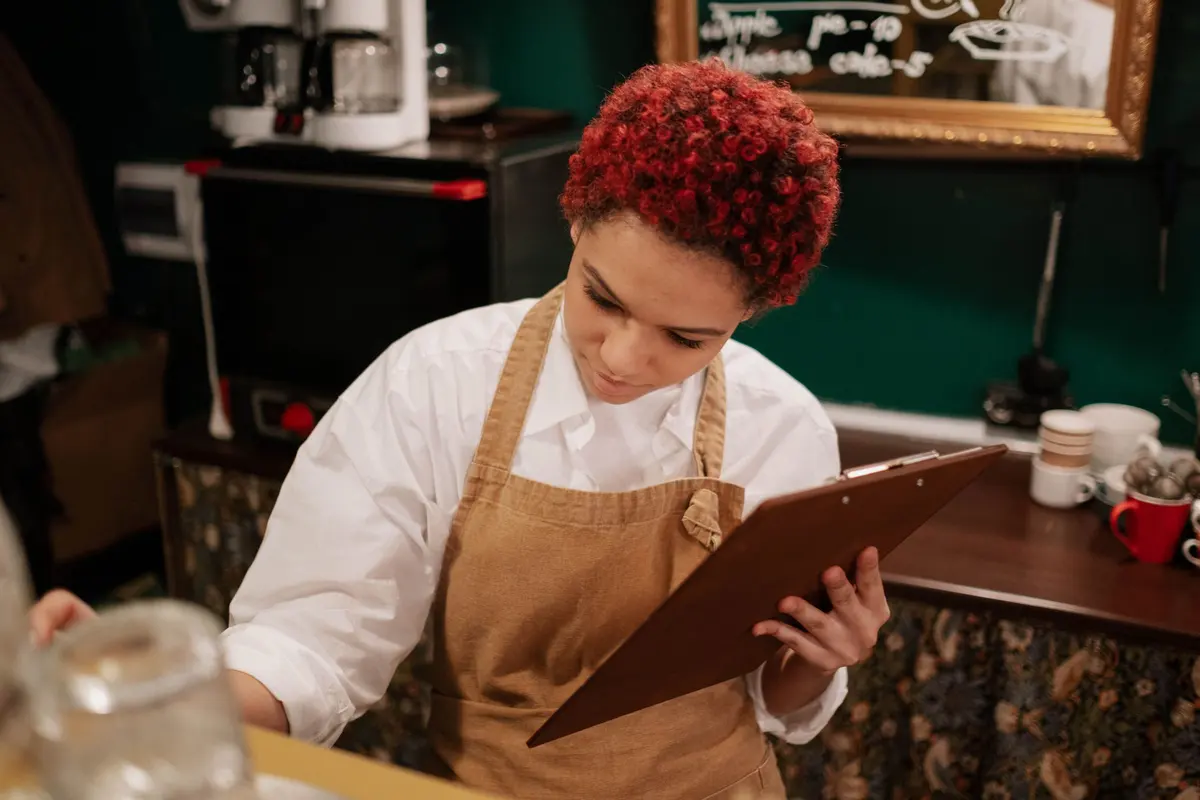Una ragazza con il grembiule compila una scheda su una cartellina, dentro un caffè