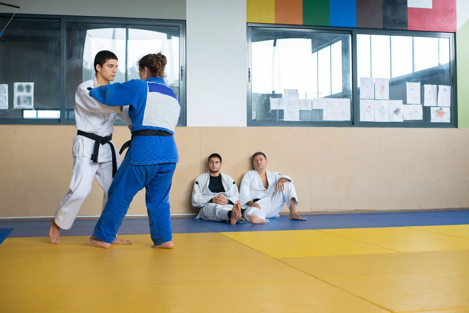 Un uomo in judogi bianco e una donna in judogi blu cercano la presa sul tatami