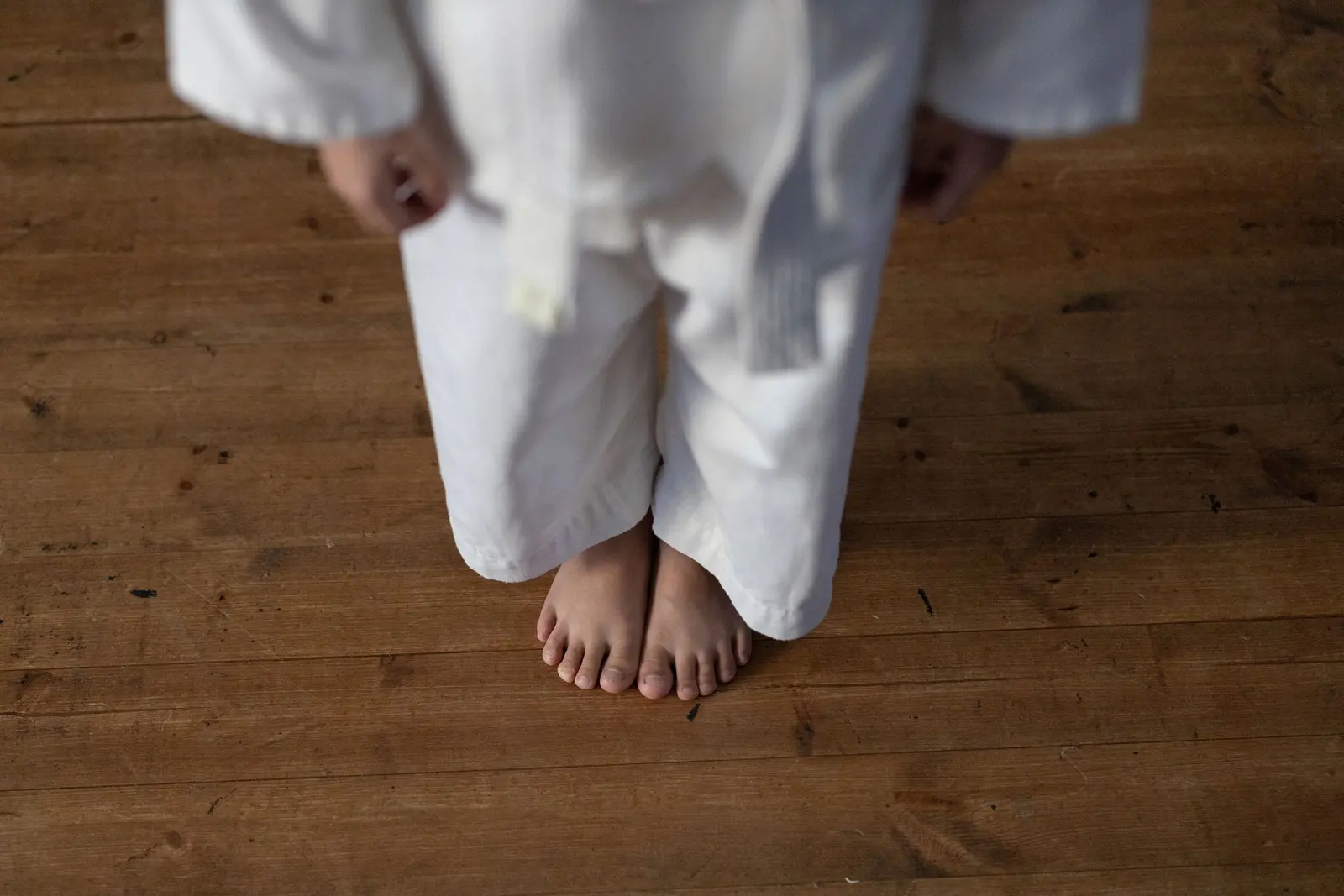 Bambino scalzo sul pavimento di legno con il gi bianco e la cintura bianca