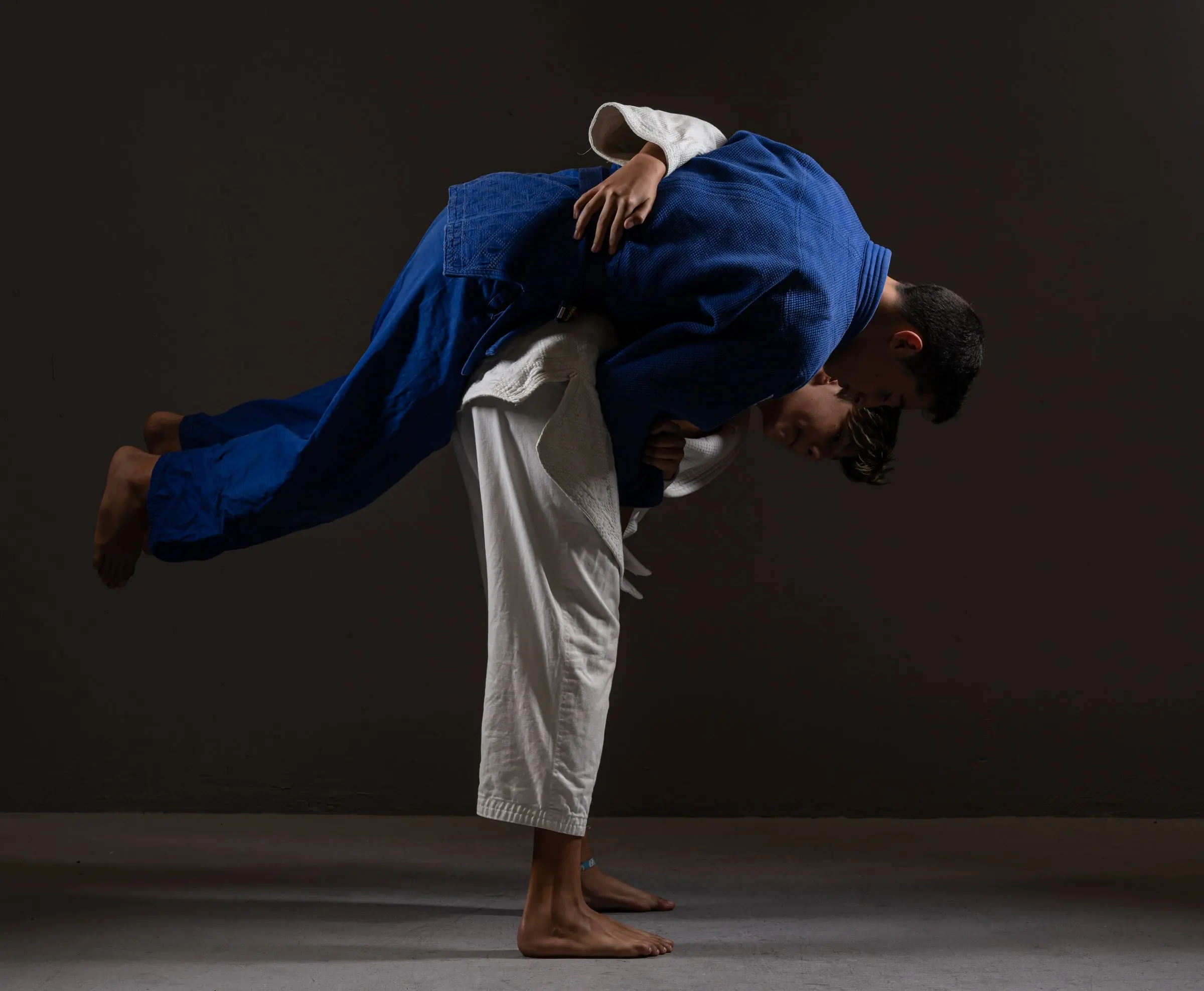 Proiezione di judo su fondo nero: un judoka in judogi bianco carica sulla schiena il compagno in judogi blu