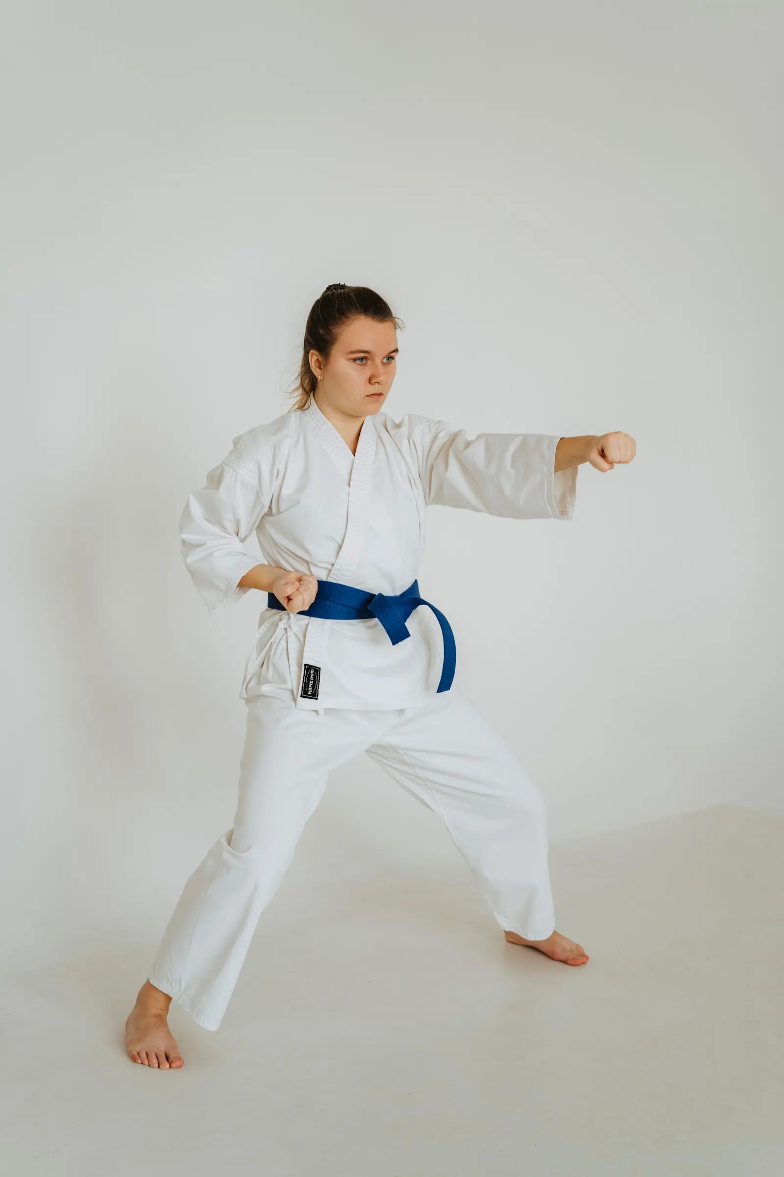 Ragazza in karategi bianco e cintura blu esegue un pugno in posizione avanzata